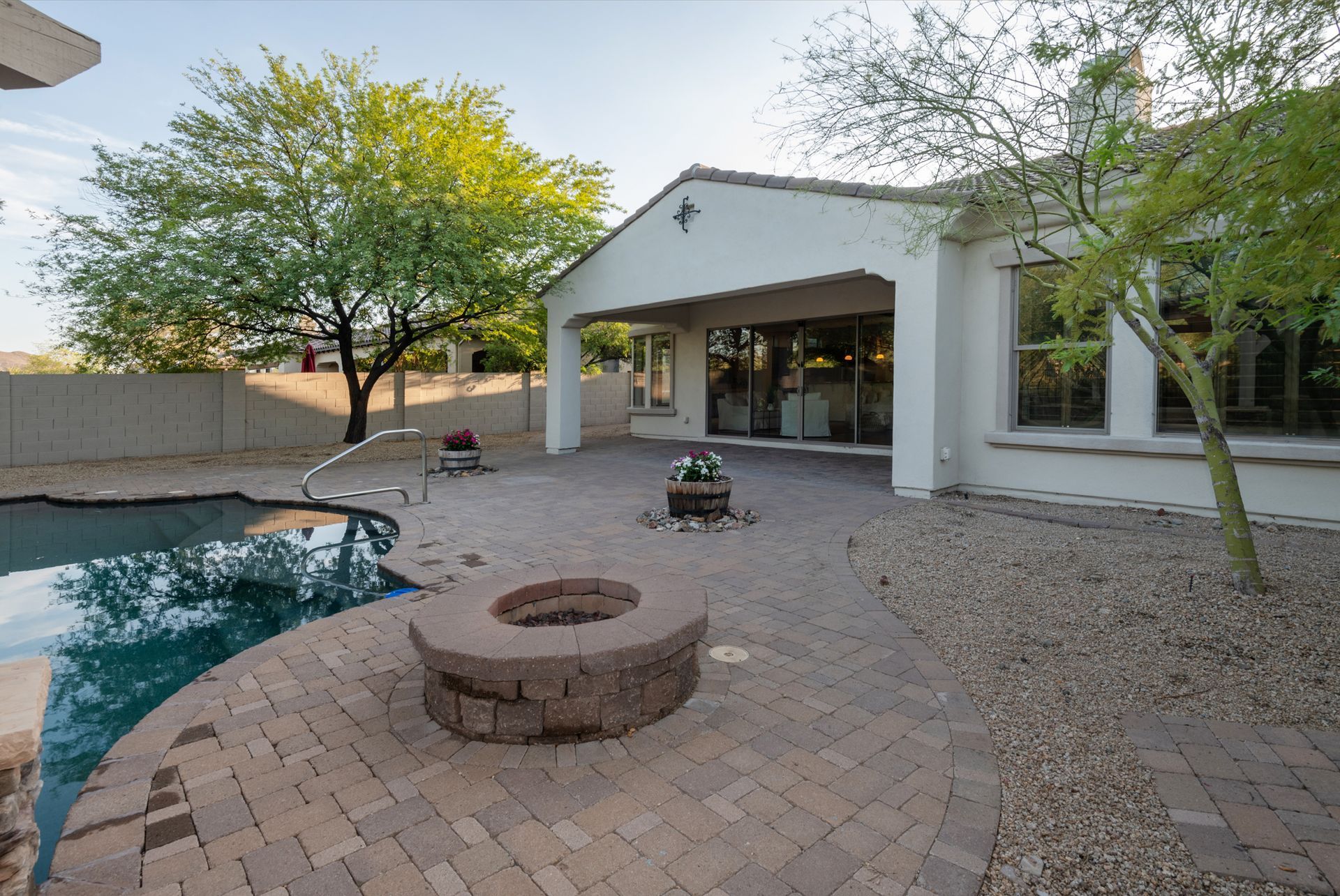 A fire pit sits on a brick patio next to a pool