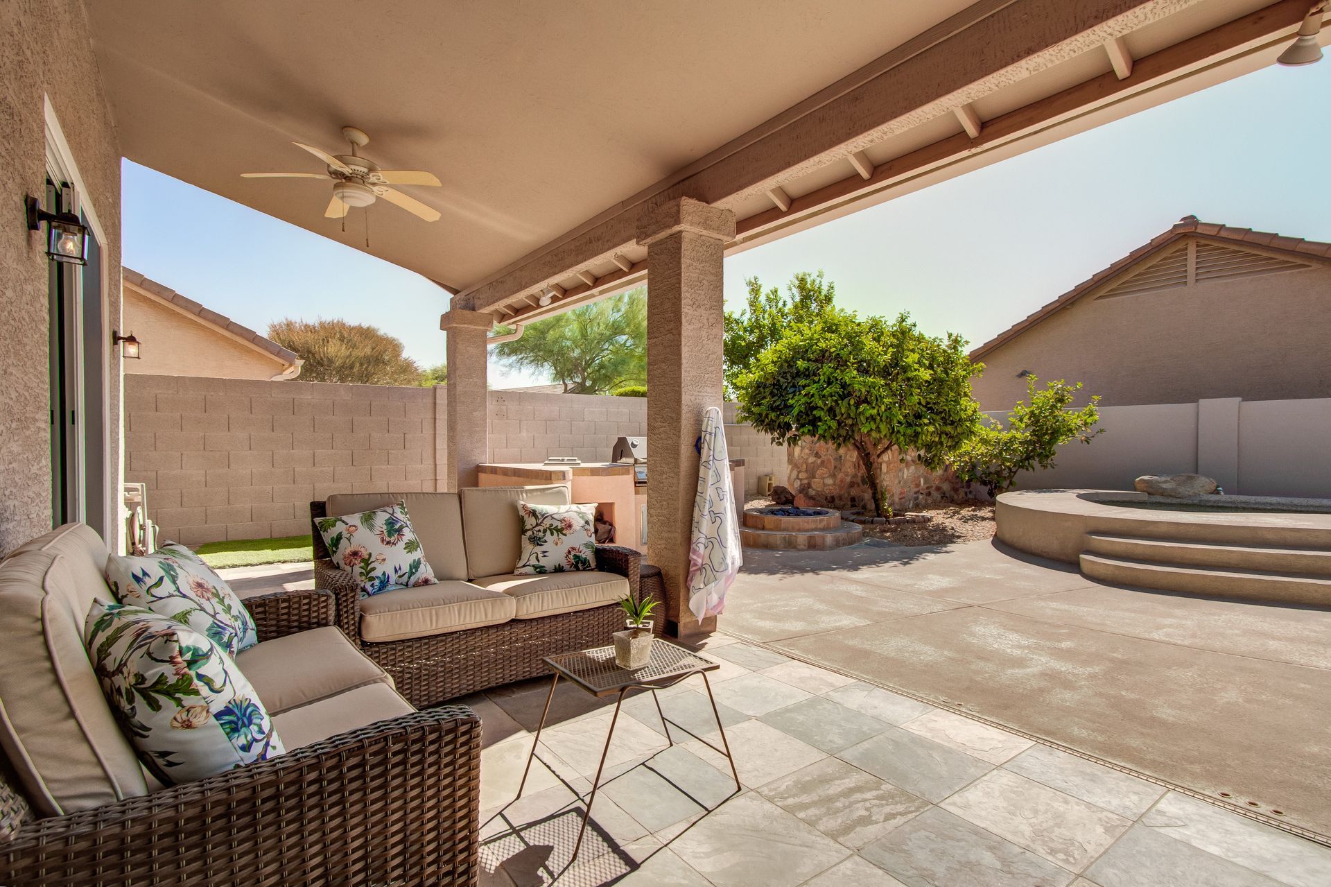 A patio with a couch and a table under a ceiling fan.