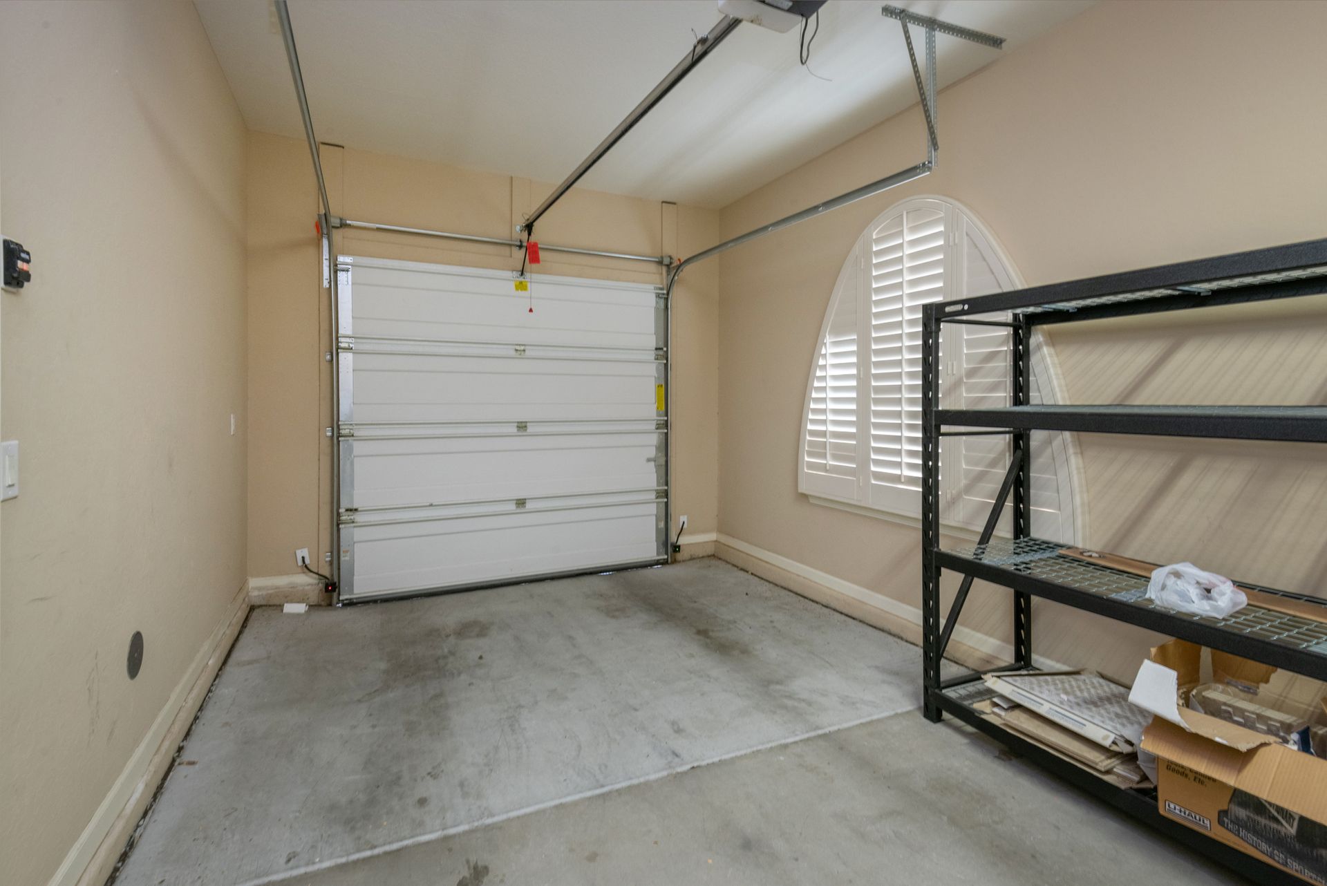 An empty garage with a garage door open and a shelving unit.