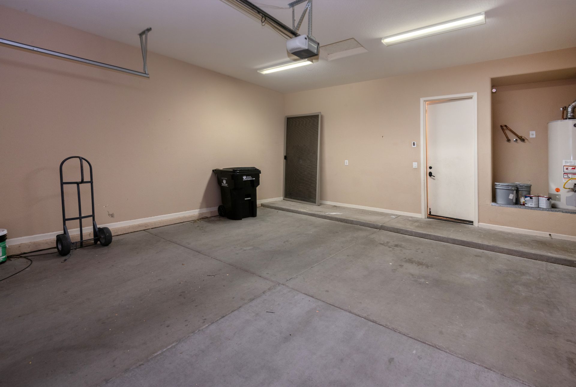 An empty garage with a trash can and a water heater