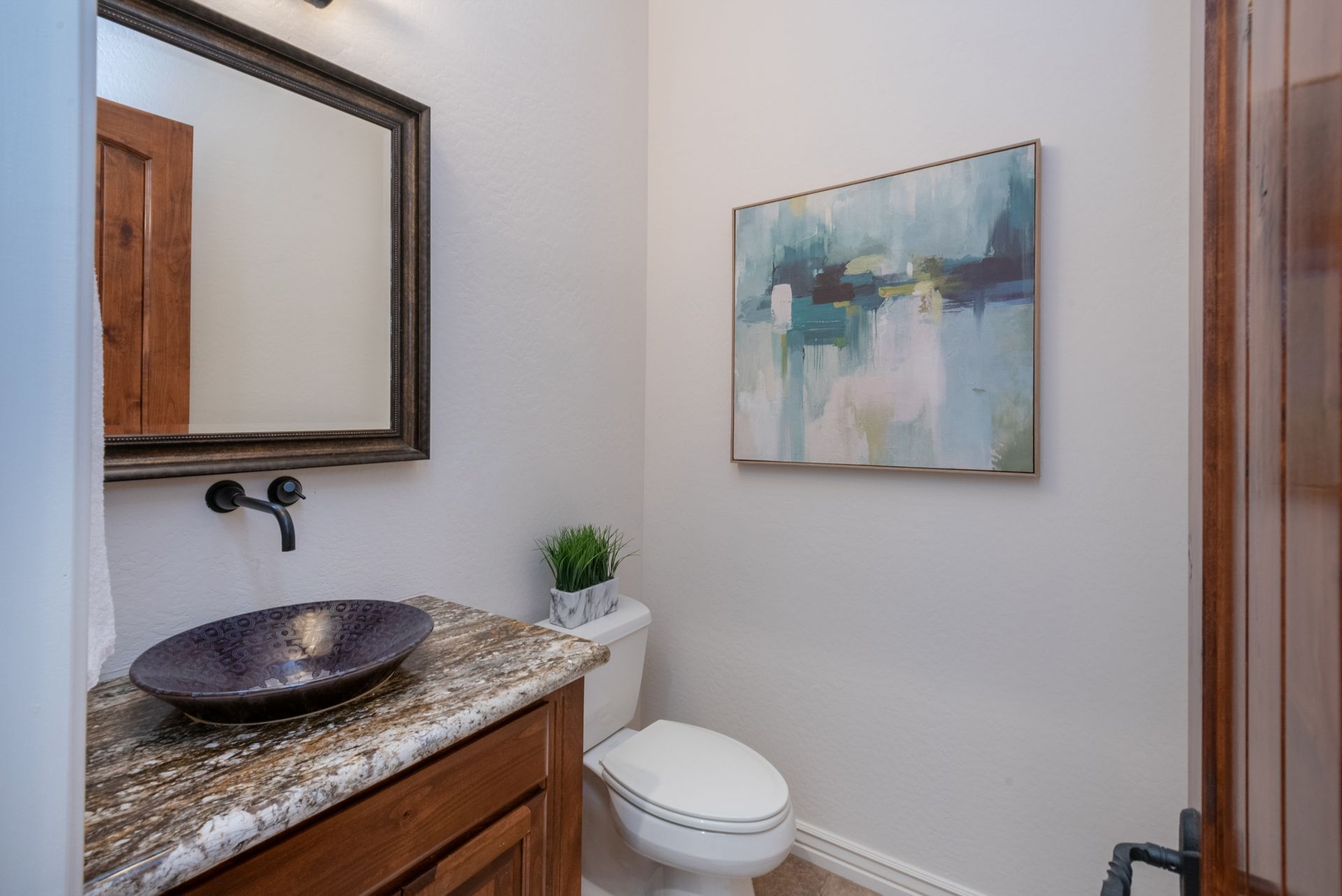A bathroom with a sink , toilet , mirror and painting on the wall.