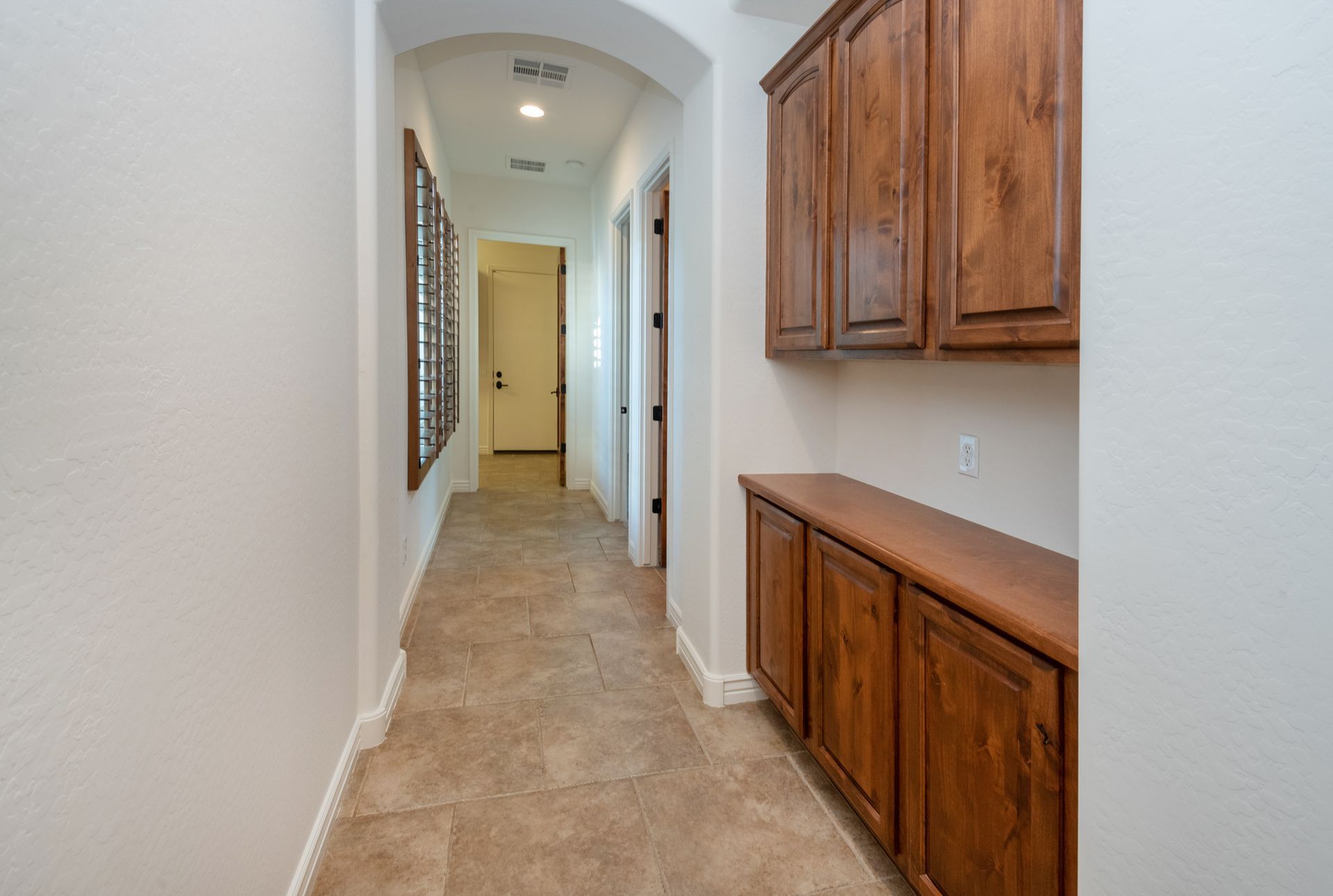 A long hallway with wooden cabinets and tile floors in a house.