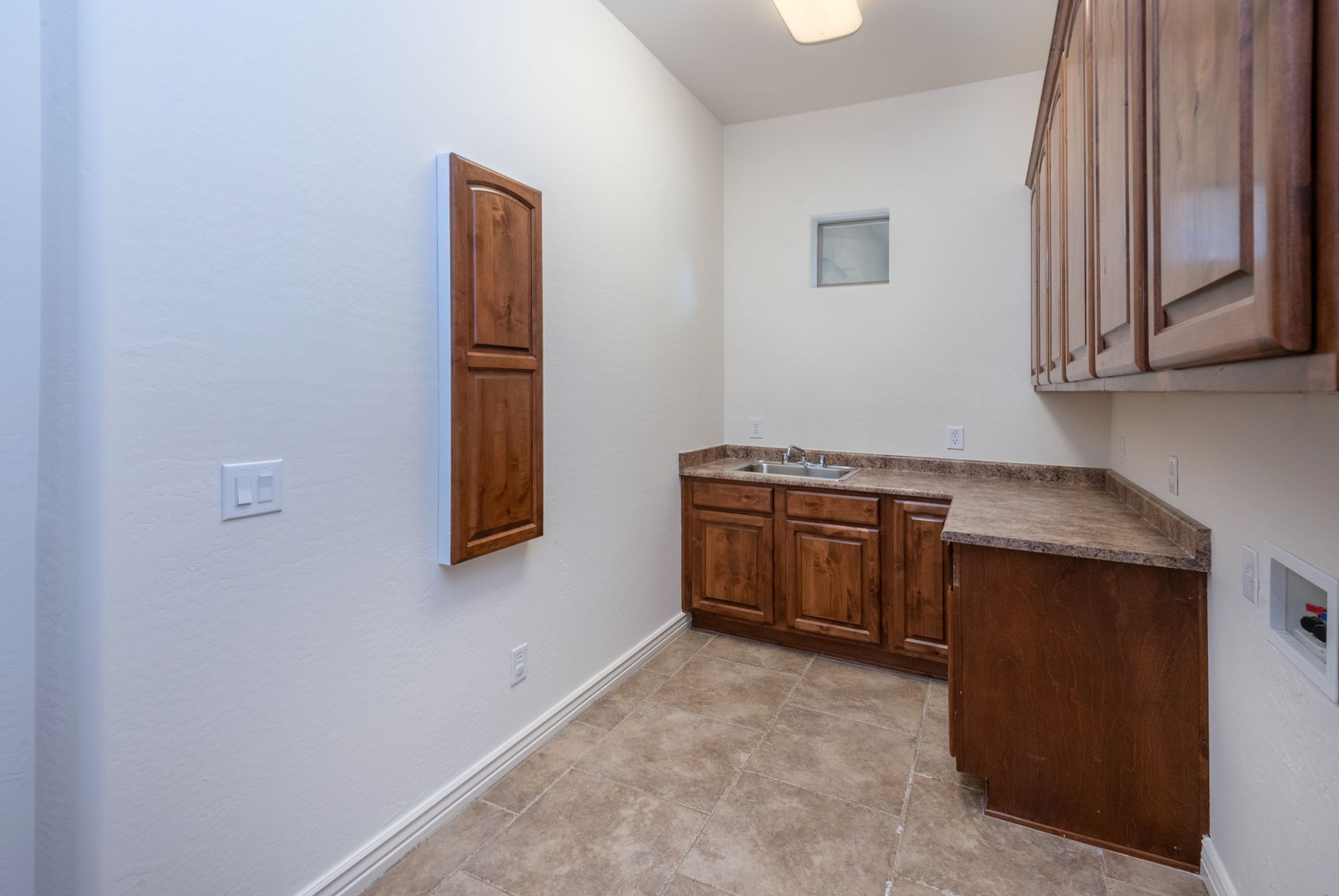 A laundry room with wooden cabinets and a sink.