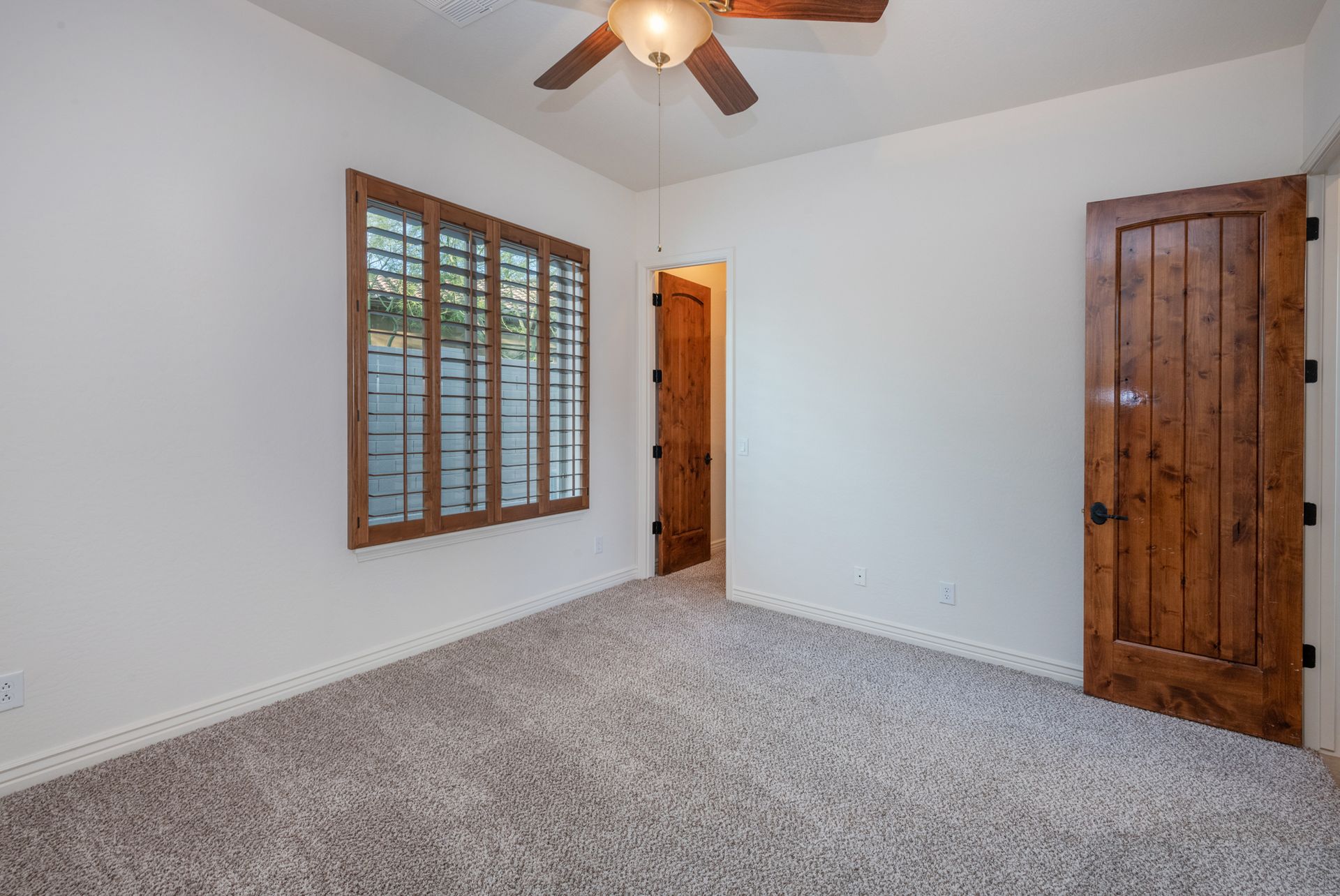 An empty bedroom with a ceiling fan and two windows.