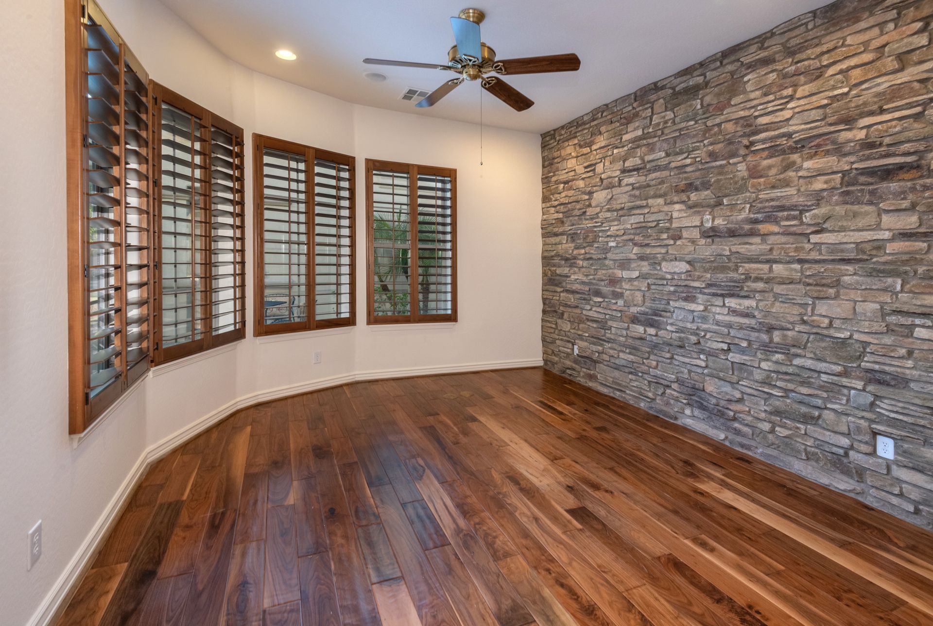 An empty room with hardwood floors , a stone wall and a ceiling fan.
