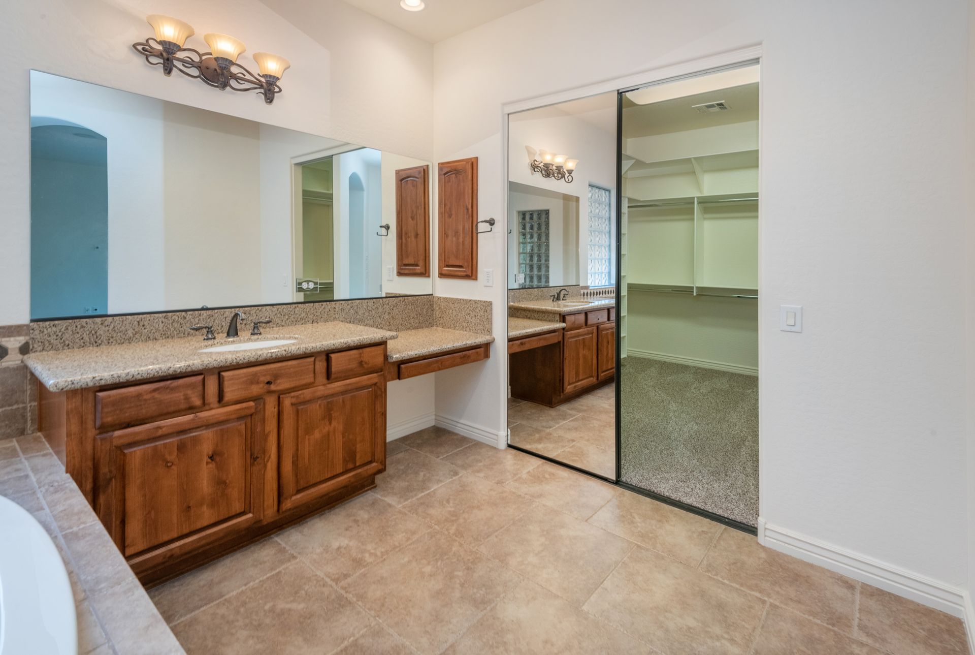 A bathroom with two sinks , two mirrors and a walk in closet.