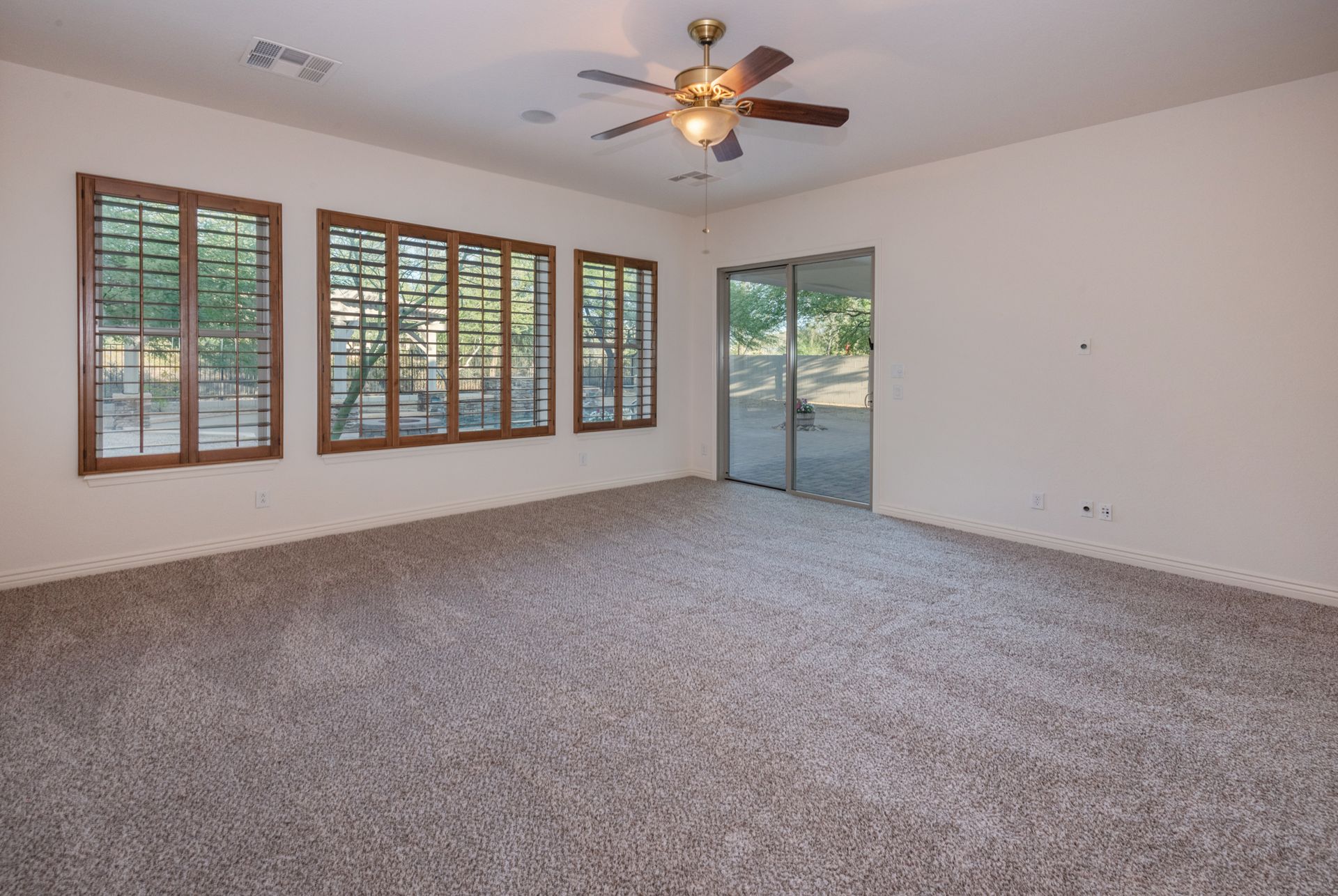 An empty living room with a ceiling fan and lots of windows.