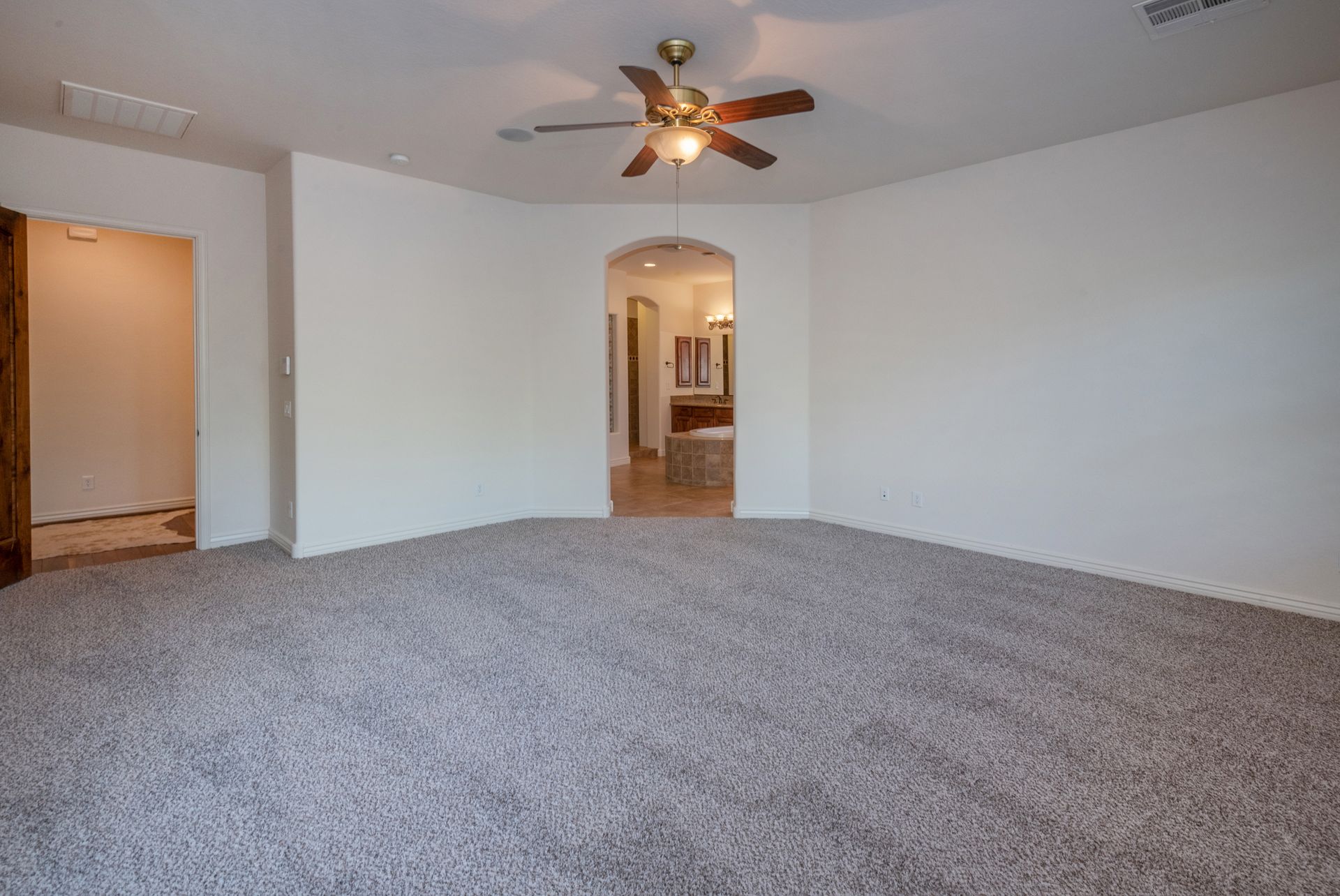 An empty living room with a ceiling fan and carpet.