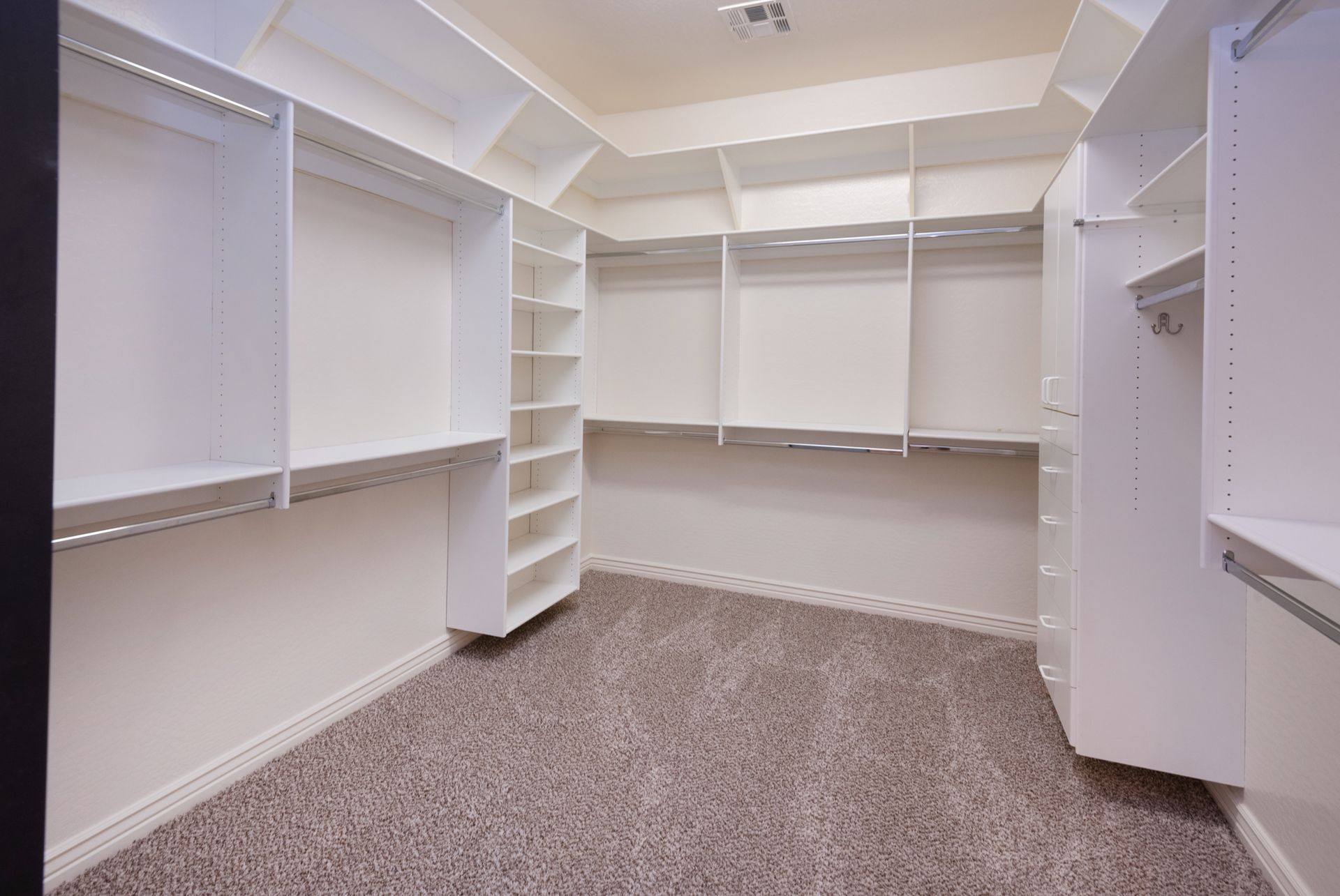 A walk in closet with white shelves and a carpeted floor.