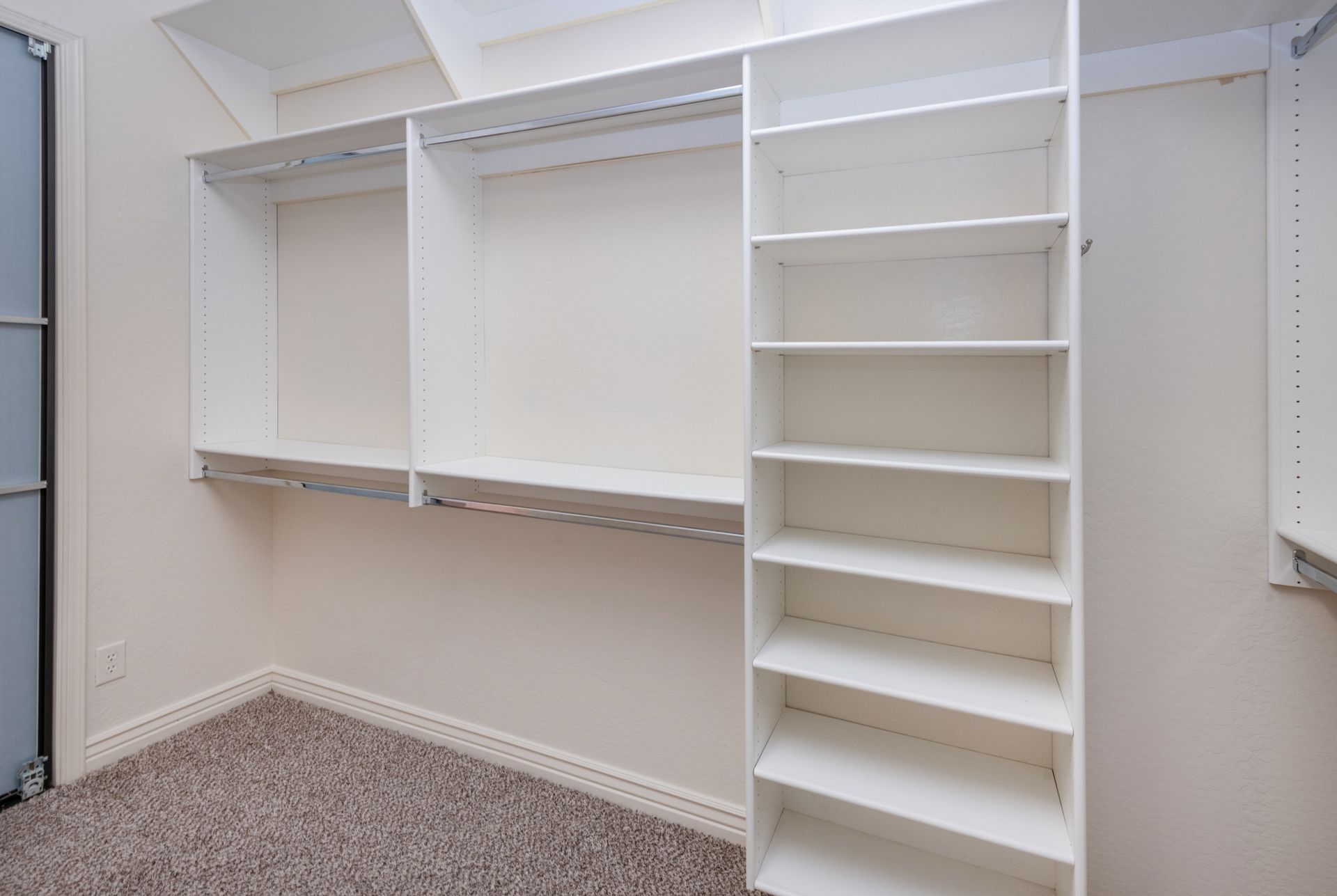 An empty walk in closet with white shelves and a carpeted floor.
