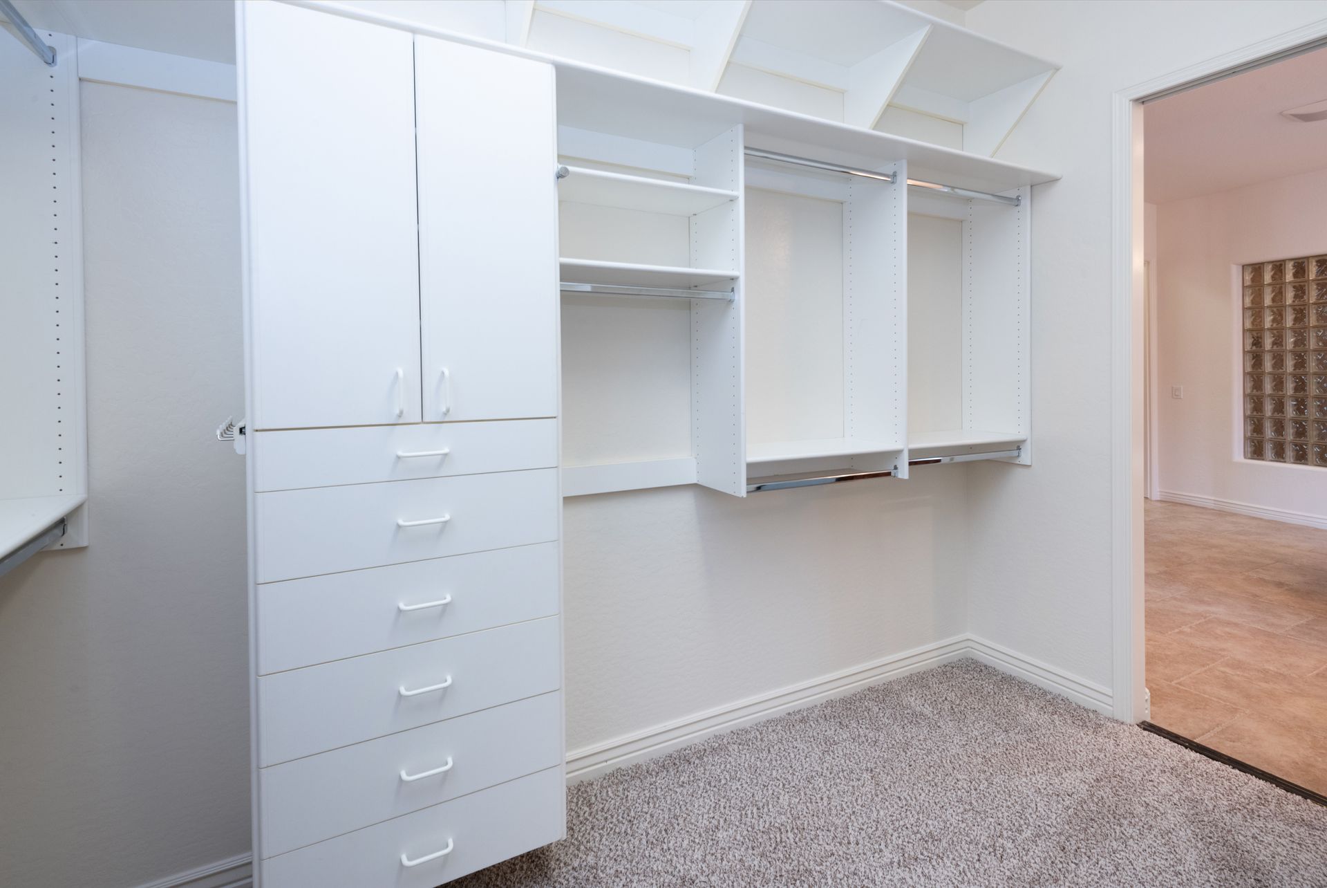 A walk in closet with white cabinets and drawers and a carpeted floor.