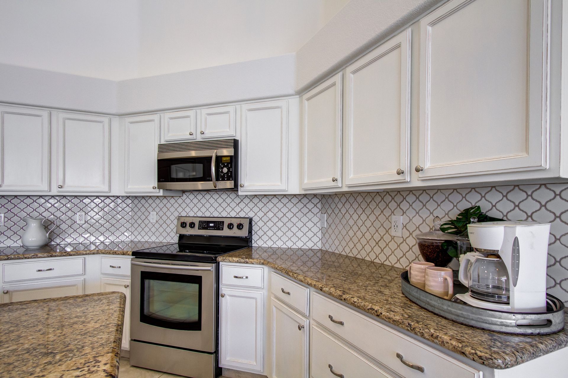 A kitchen with white cabinets , stainless steel appliances , granite counter tops and a coffee maker.
