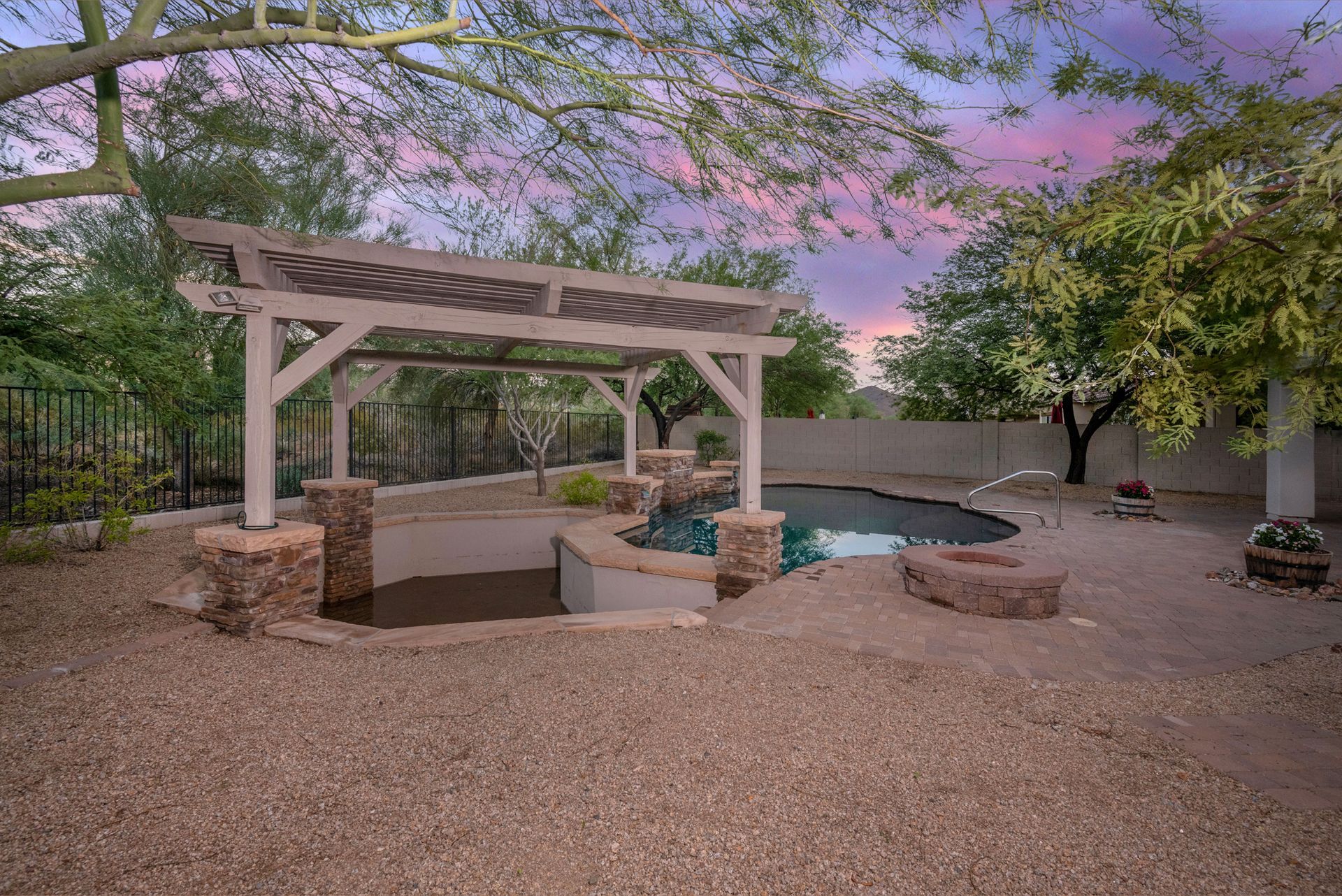 A large swimming pool with a pergola in the backyard at sunset.