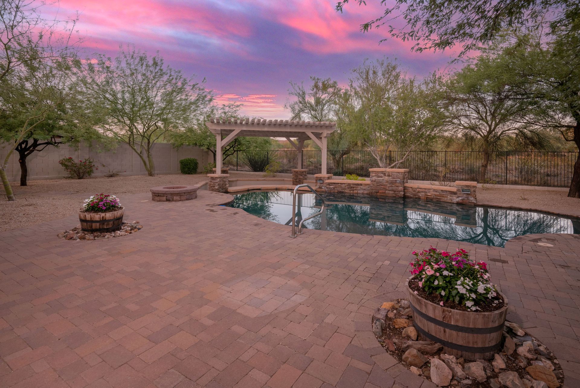 A large swimming pool with a pergola in the backyard at sunset.