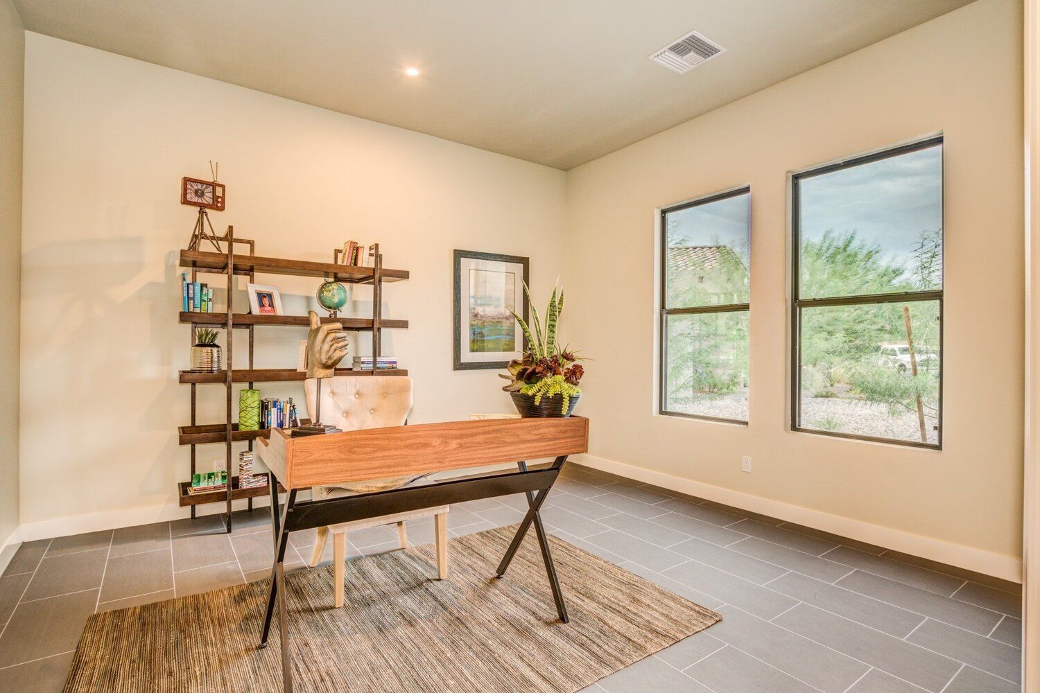 A home office with a desk , chair , bookshelf and windows.
