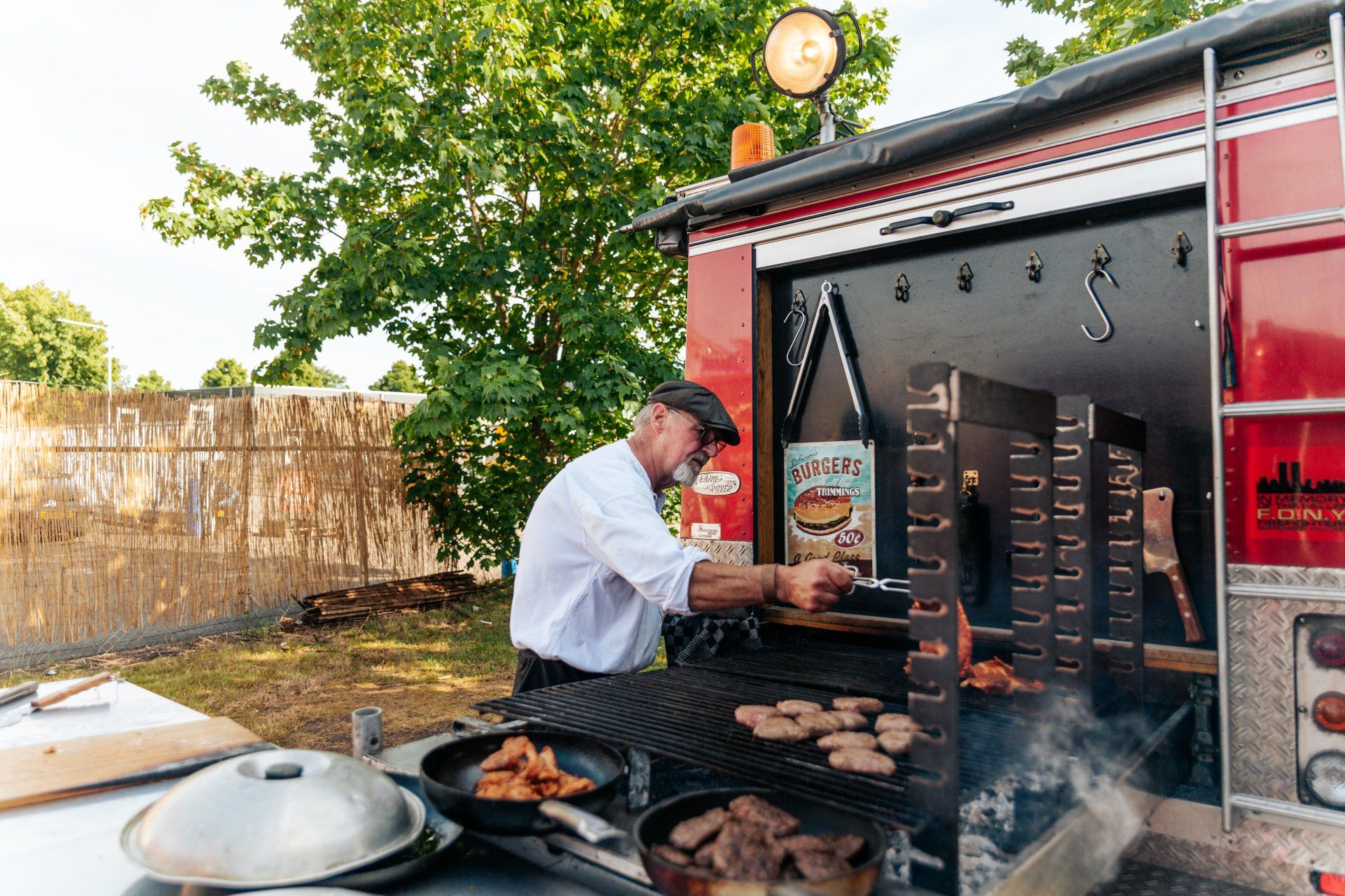 Een man grilt buiten op een speciaal ontworpen rode brandweerwagengrill; er stijgt rook op uit de grill.