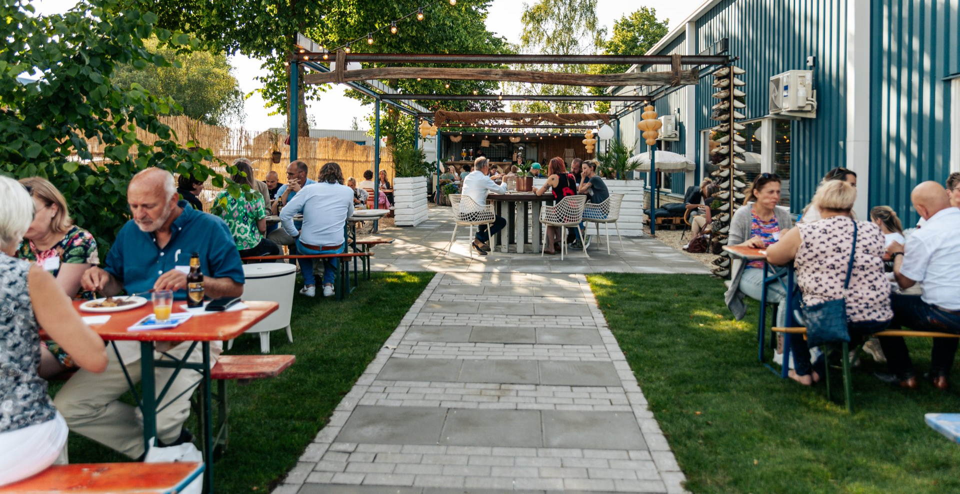 Buitenpatio met mensen die aan het dineren zijn, tafels en een pergola.