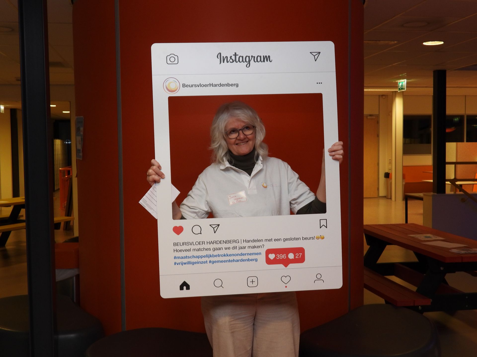 Vrouw met een Instagram-fotolijst in haar hand, staand tegen een rode muur.