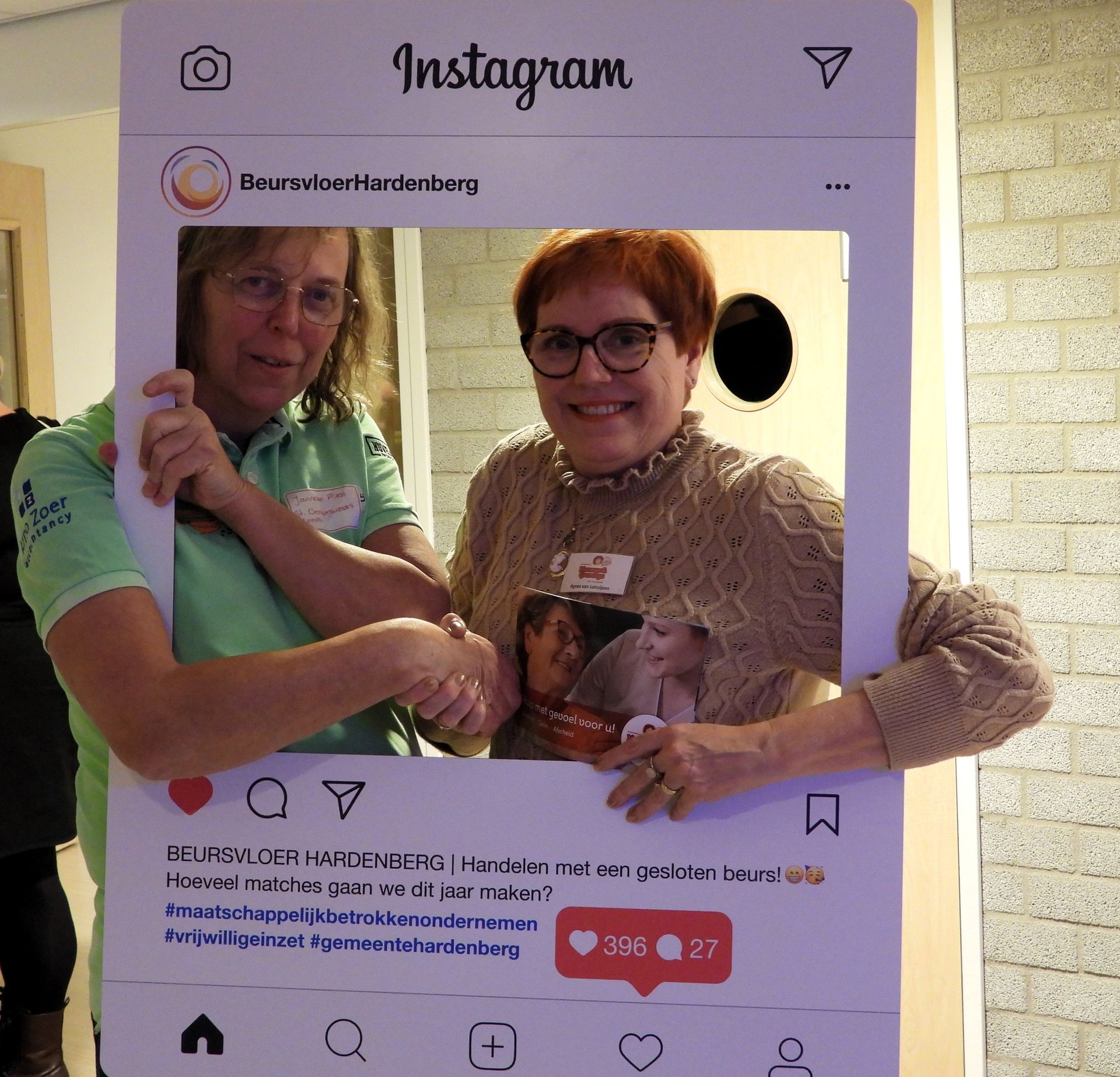 Twee vrouwen poseren voor een Instagramfoto, schudden elkaar de hand en houden een boekje vast.