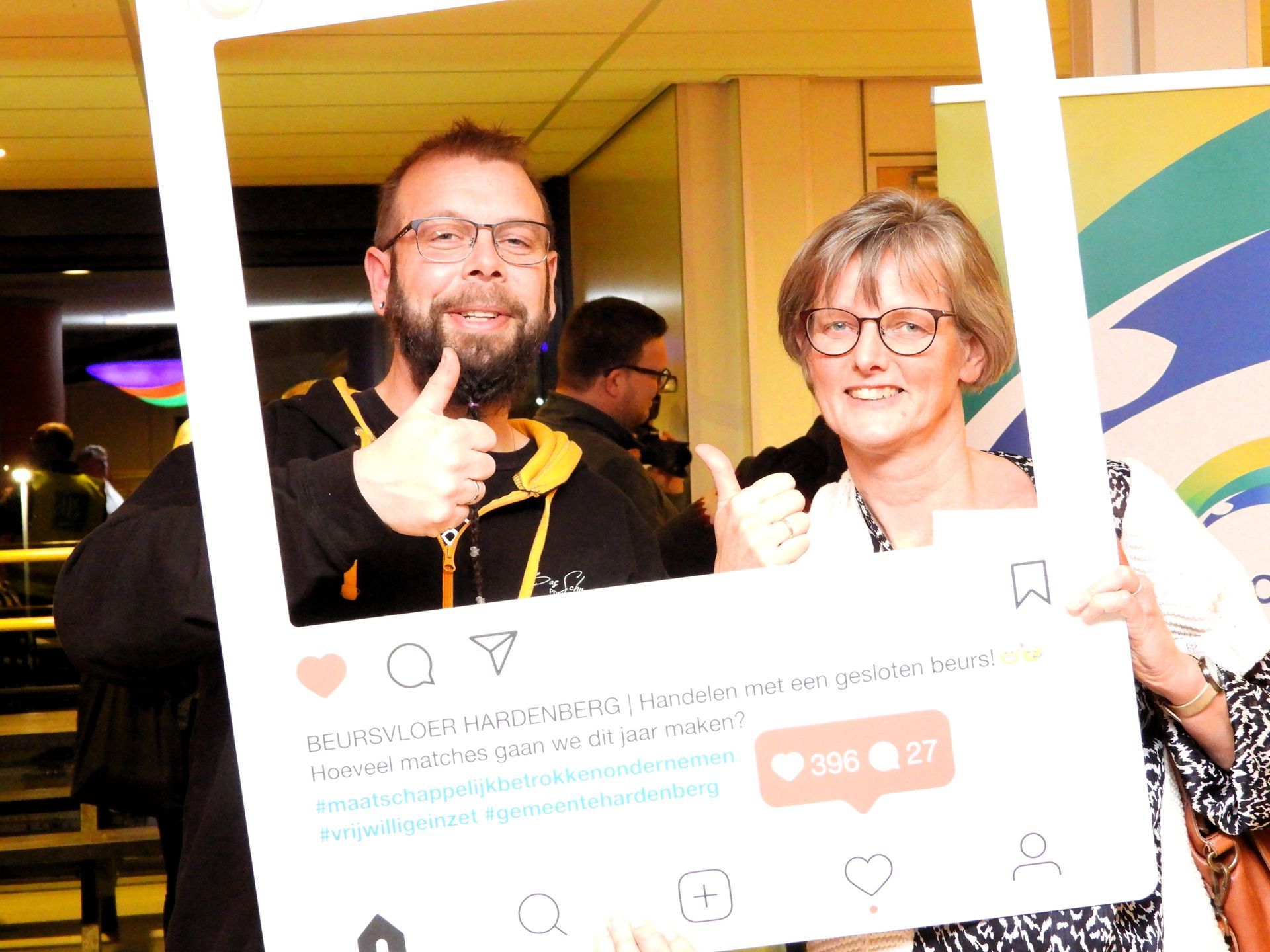 Twee mensen poseren met een extra groot Instagram-frame, lachend en met een duim omhoog.