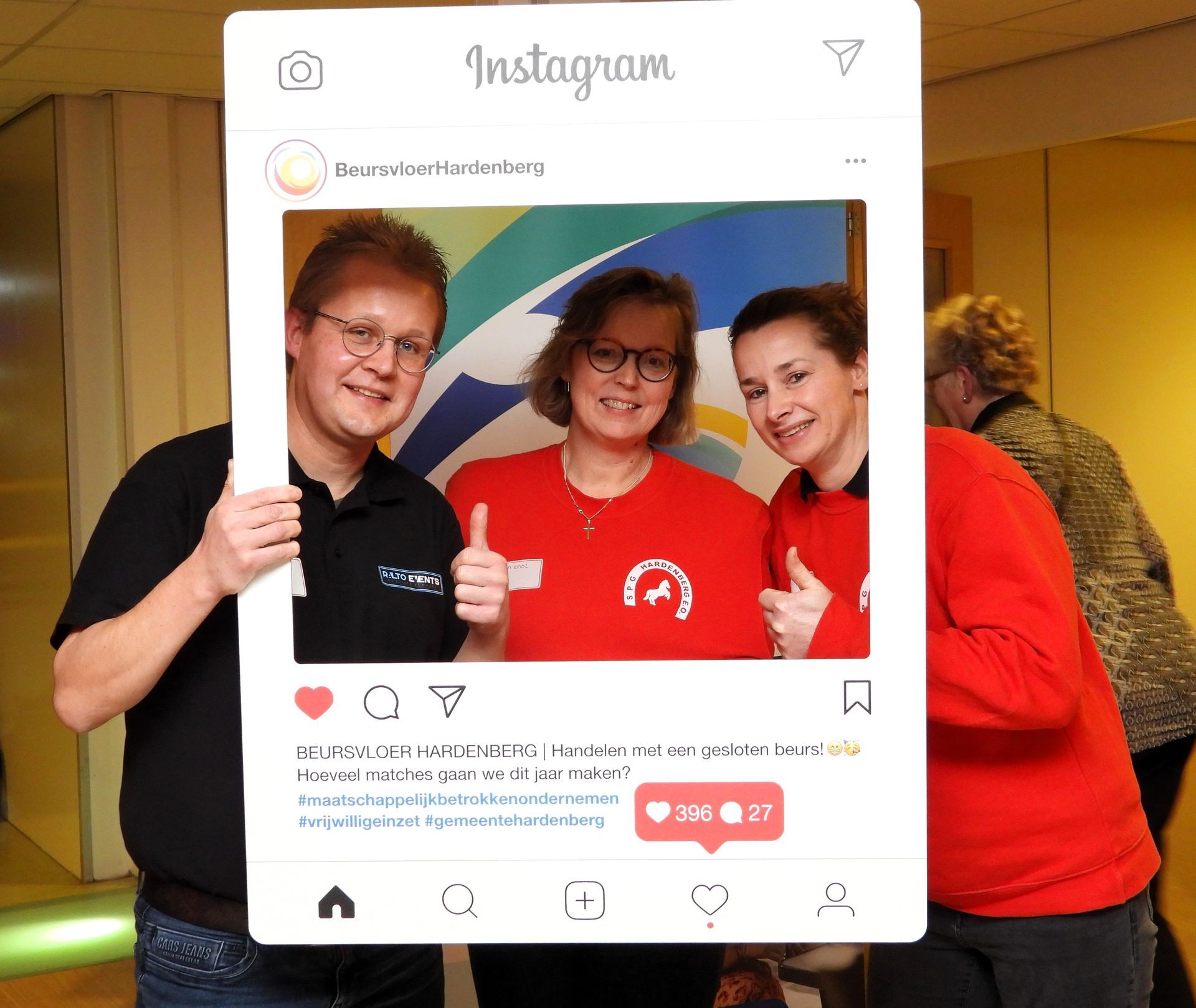Drie mensen poseren met een Instagram-fotolijstje, met hun duimen omhoog, binnen.