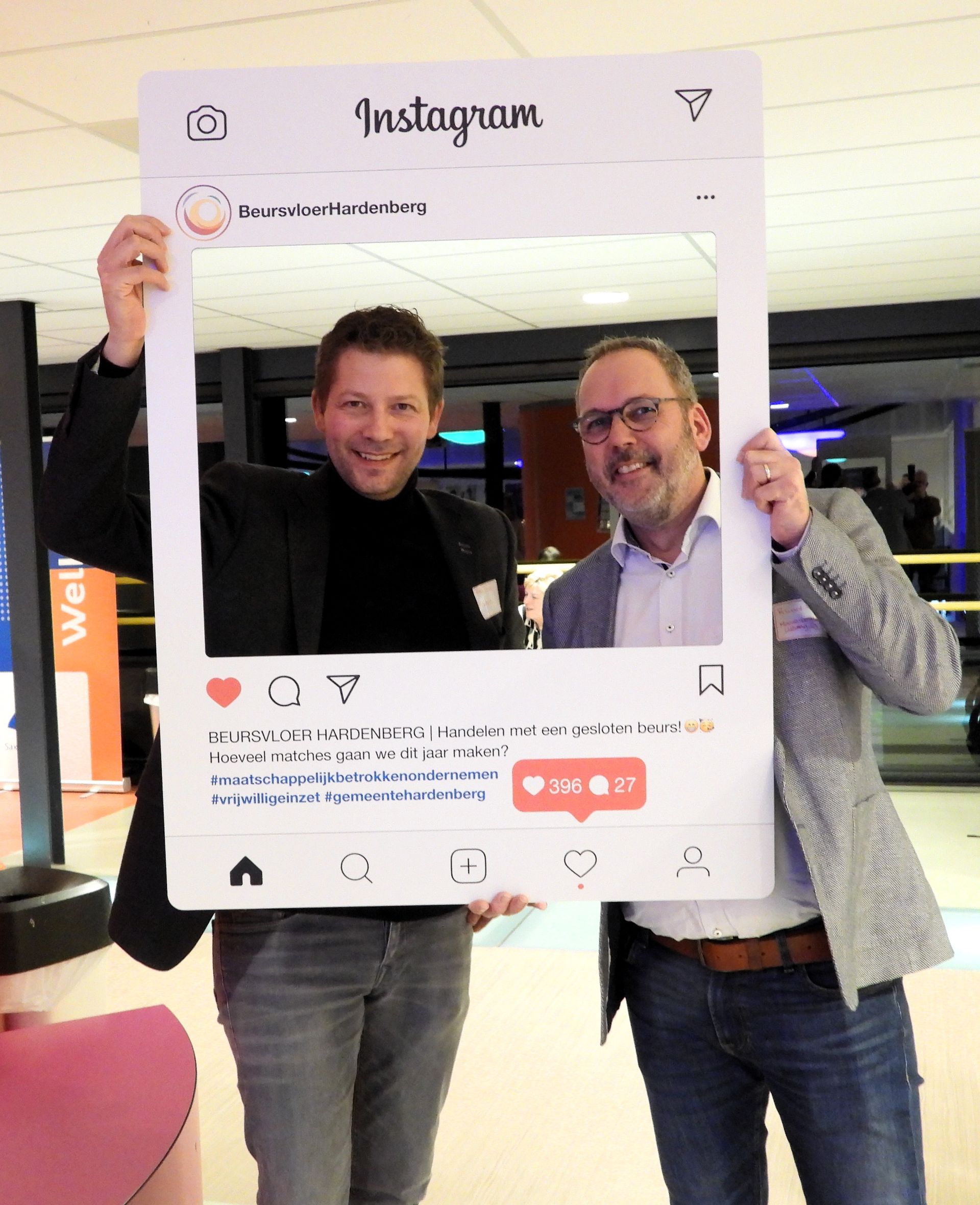 Twee mannen poseren lachend met een grote Instagram-fotolijst in een binnenruimte.