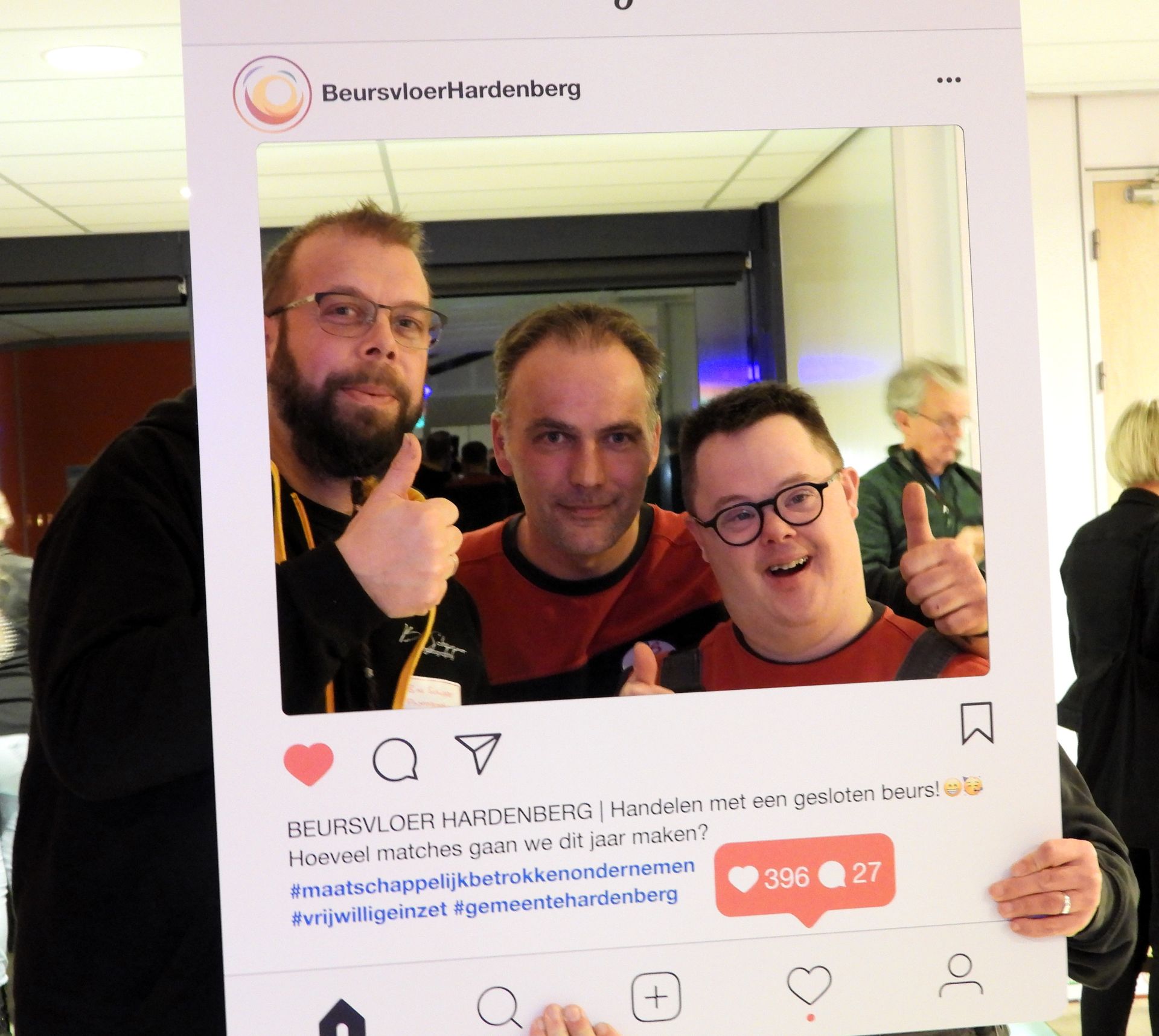 Drie mannen glimlachen en steken hun duim omhoog terwijl ze poseren voor een foto die bedoeld is voor sociale media, tijdens een evenement.