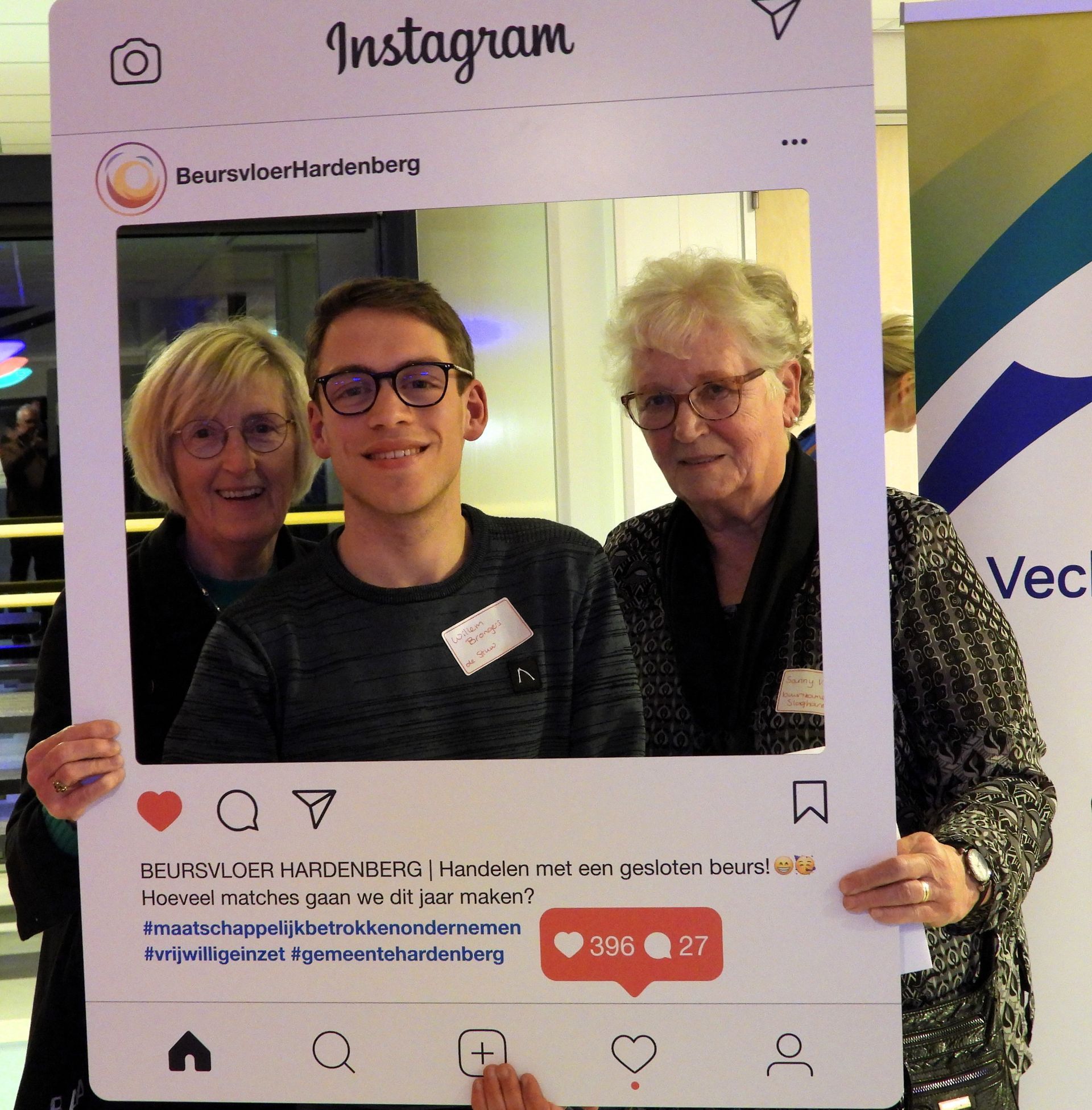 Drie mensen poseren voor een groot Instagram-frame. Twee oudere vrouwen en een jongere man glimlachen binnen het kader.