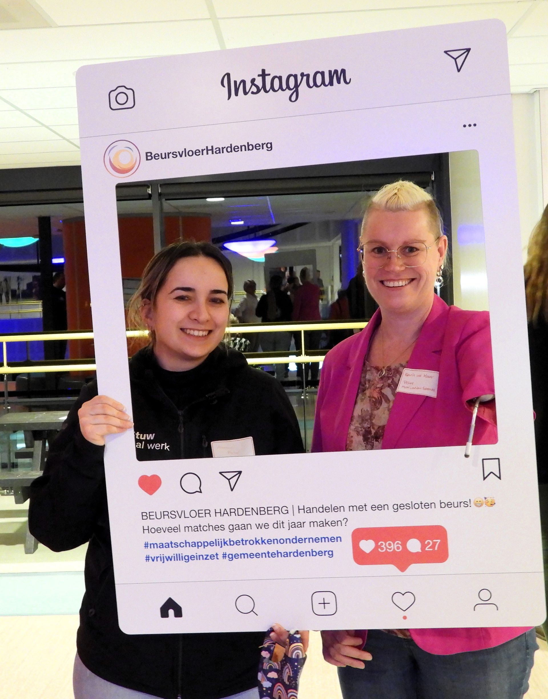 Twee vrouwen poseren lachend met een grote Instagram-fotolijst in een felverlichte ruimte.