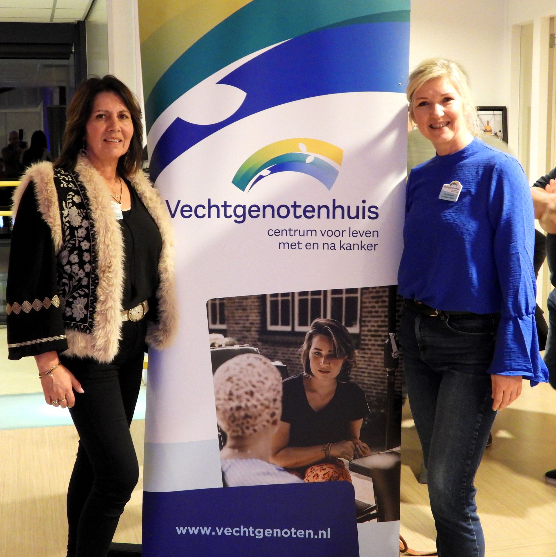 Twee vrouwen staan ​​naast een spandoek. Op het spandoek staat 