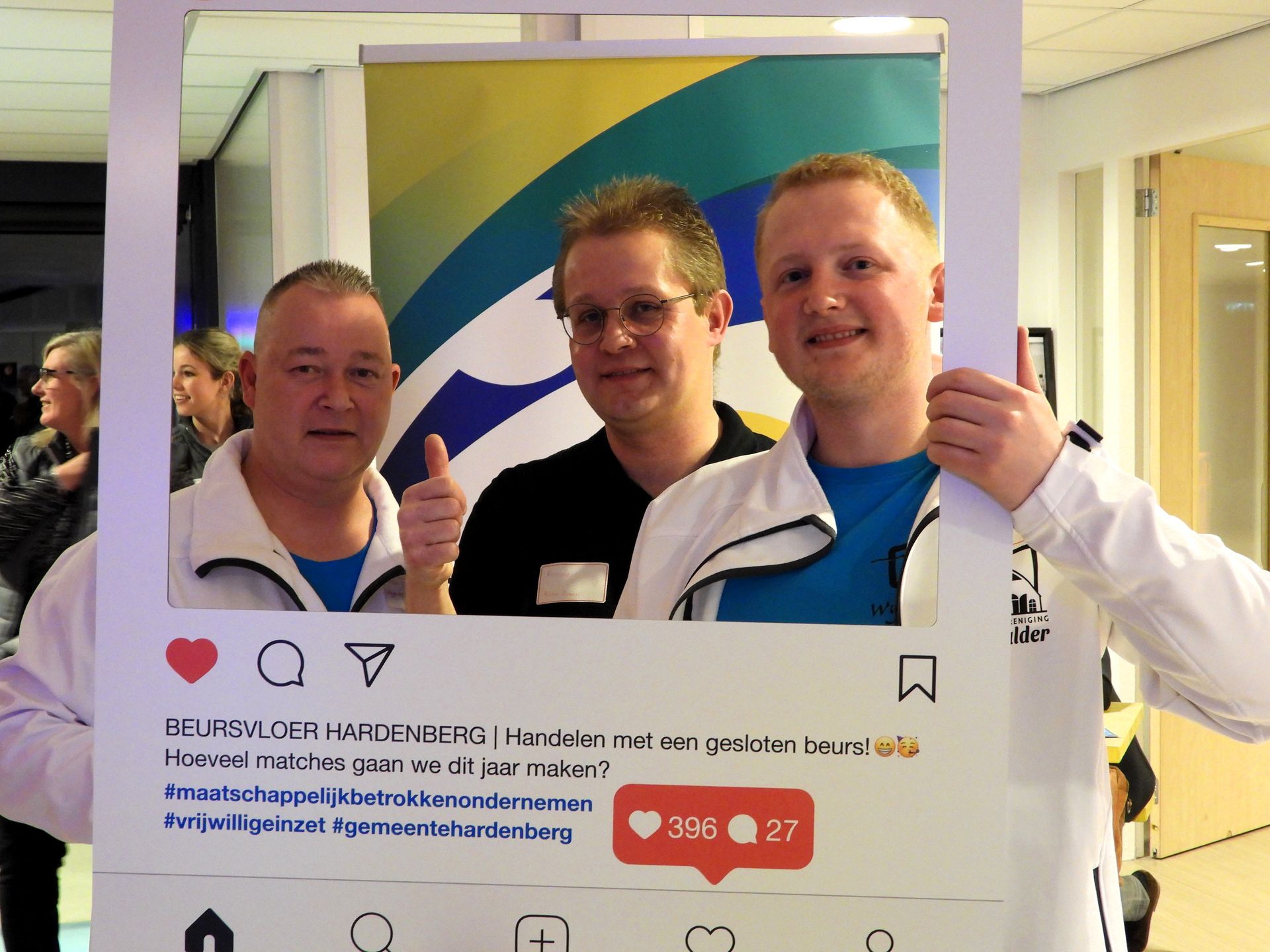 Drie mannen poseren in een Instagram-frame en steken hun duim omhoog. Op de achtergrond is een spandoek te zien.