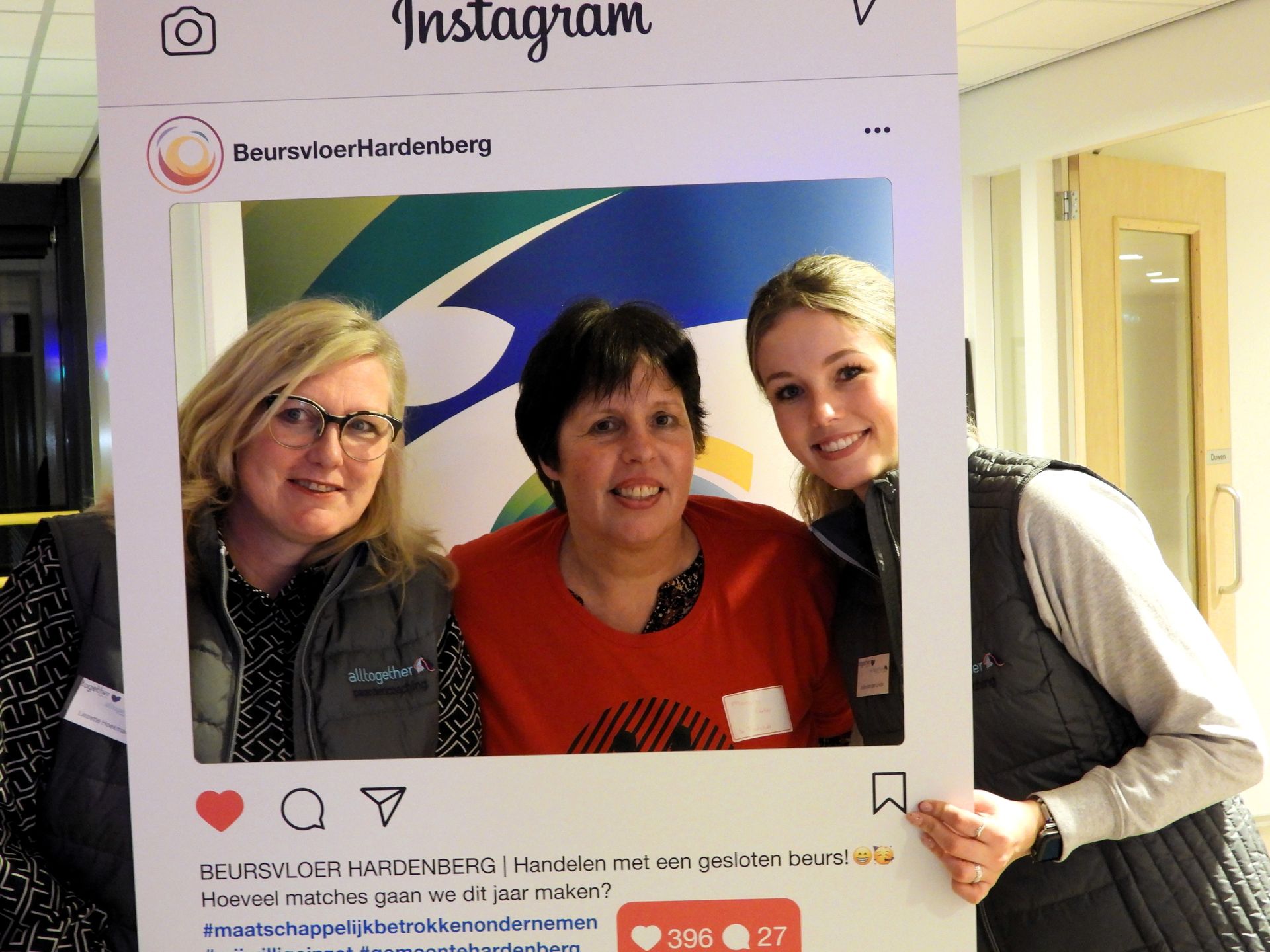 Drie mensen glimlachen op een Instagramfoto, poserend voor een spandoek.