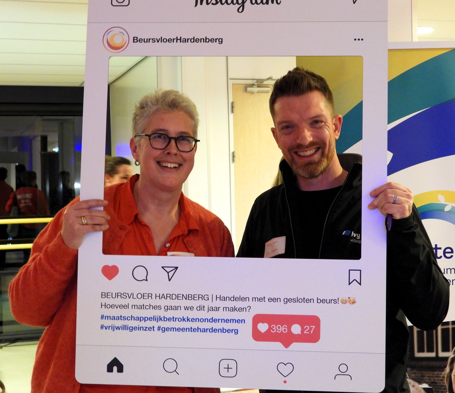 Twee mensen glimlachen, omlijst door een grote Instagram-uitsnede. De vrouw draagt ​​een bril en een oranje shirt; de man draagt ​​een zwarte jas.