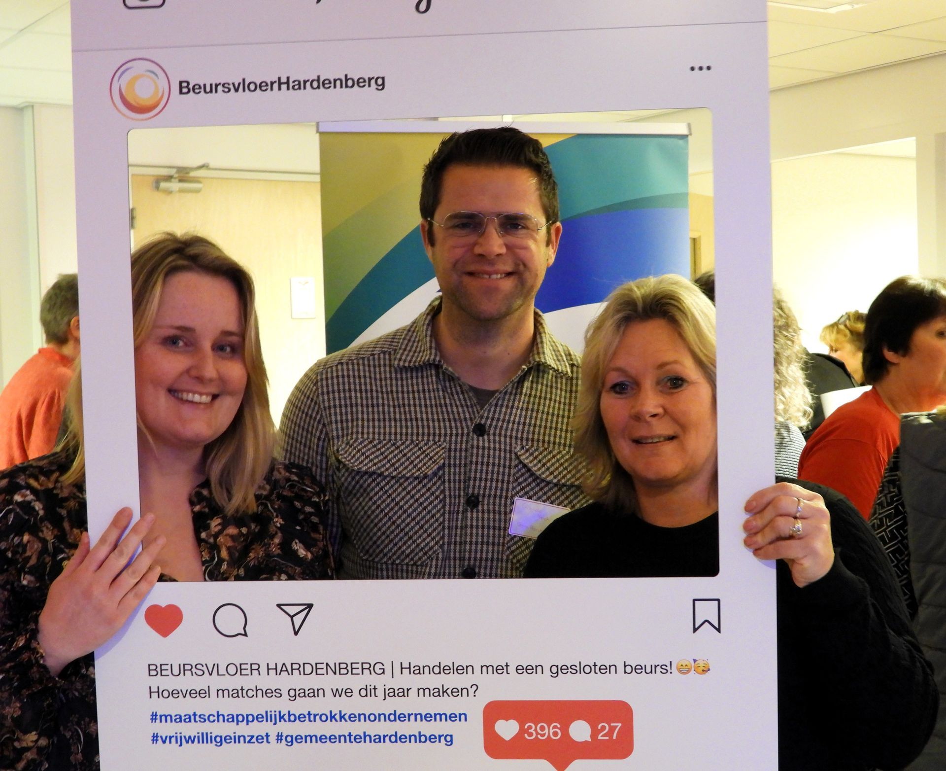 Drie mensen poseren achter een groot Instagram-frame. Twee vrouwen en een man glimlachen. Binnenlocatie.
