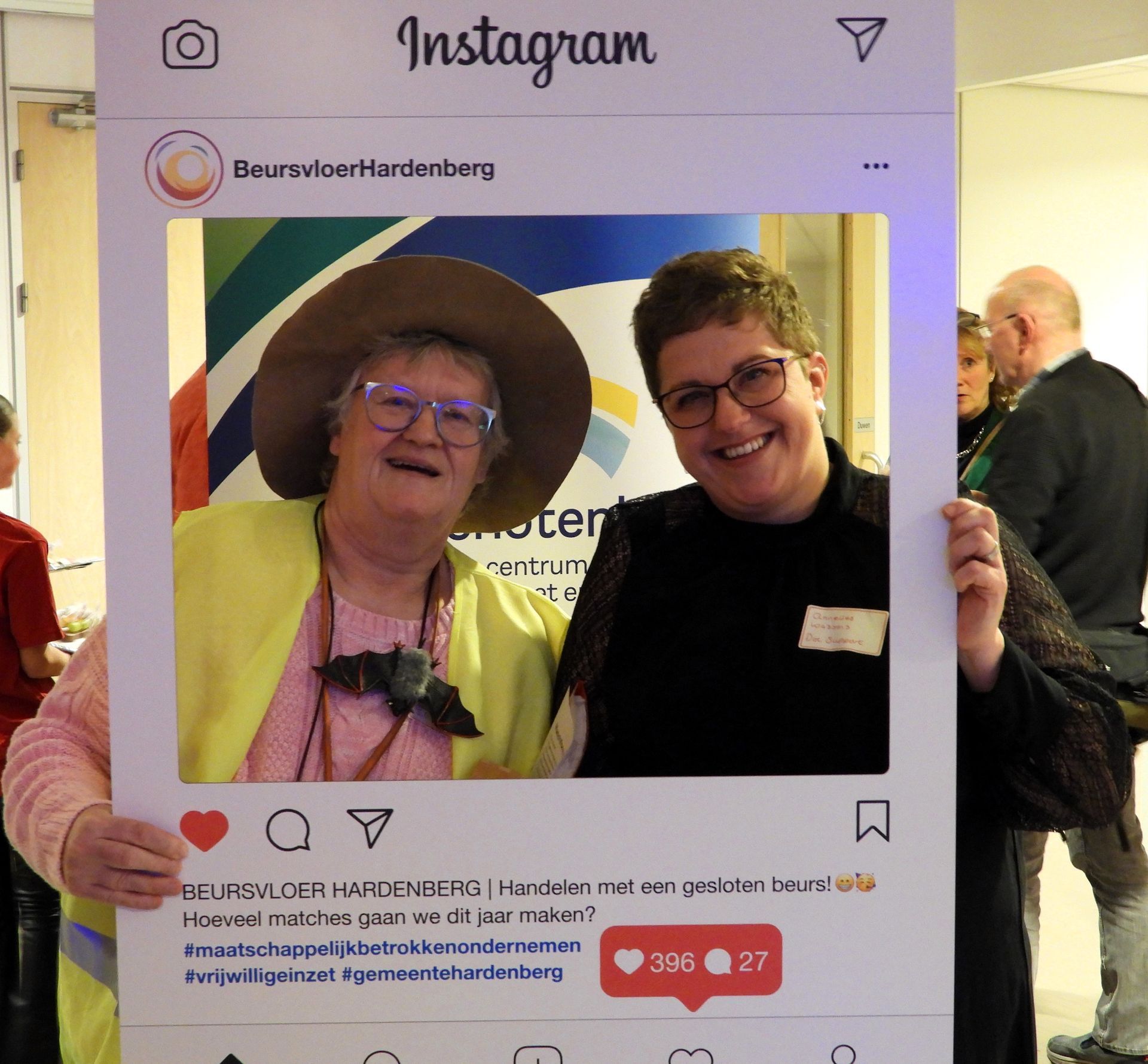 Twee mensen glimlachen voor een Instagram-frame. De een draagt ​​een hoed, de ander een bril.