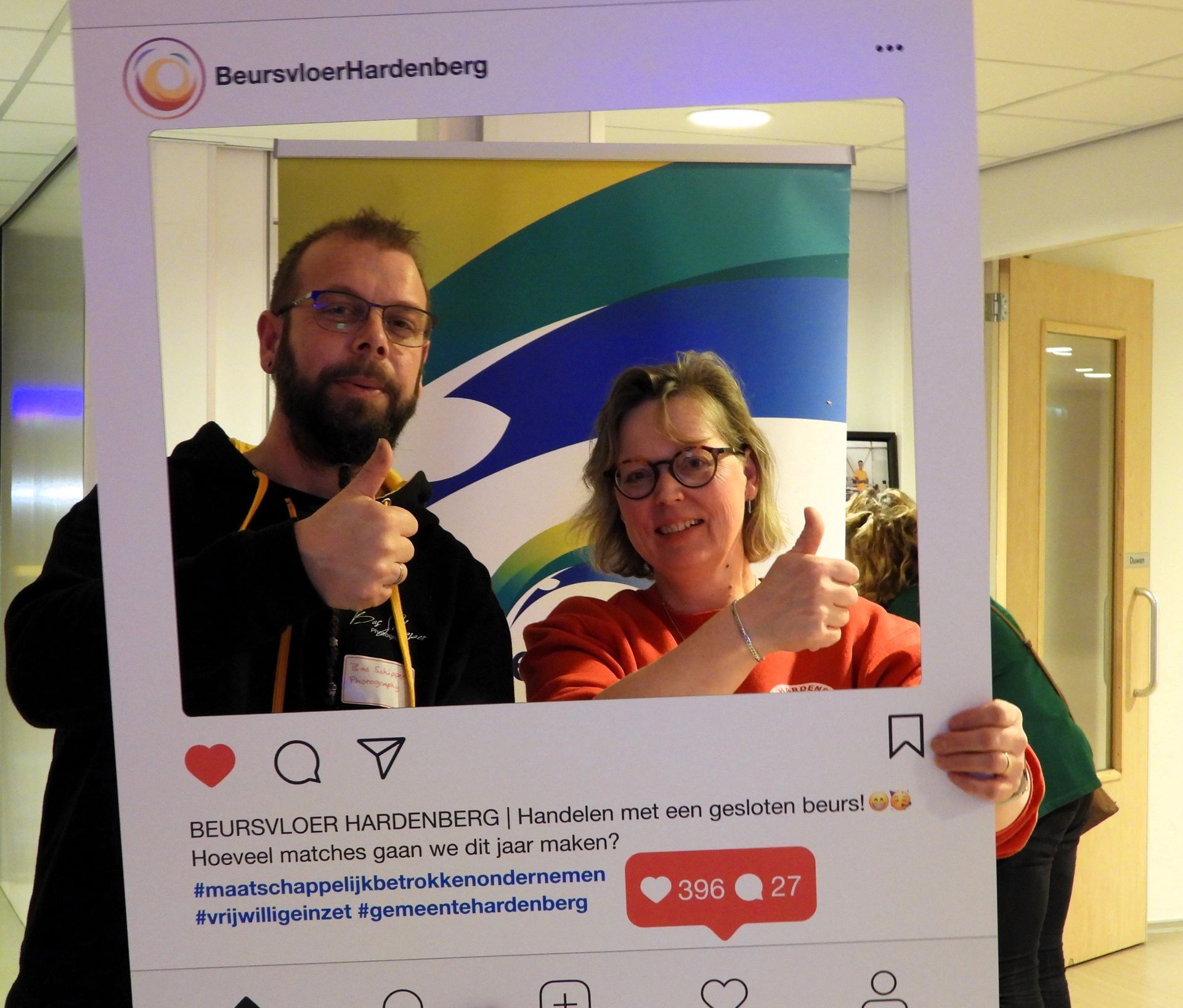 Twee mensen met een duim omhoog in een kartonnen frame voor sociale media. Op de achtergrond staan ​​een logo en een banner.