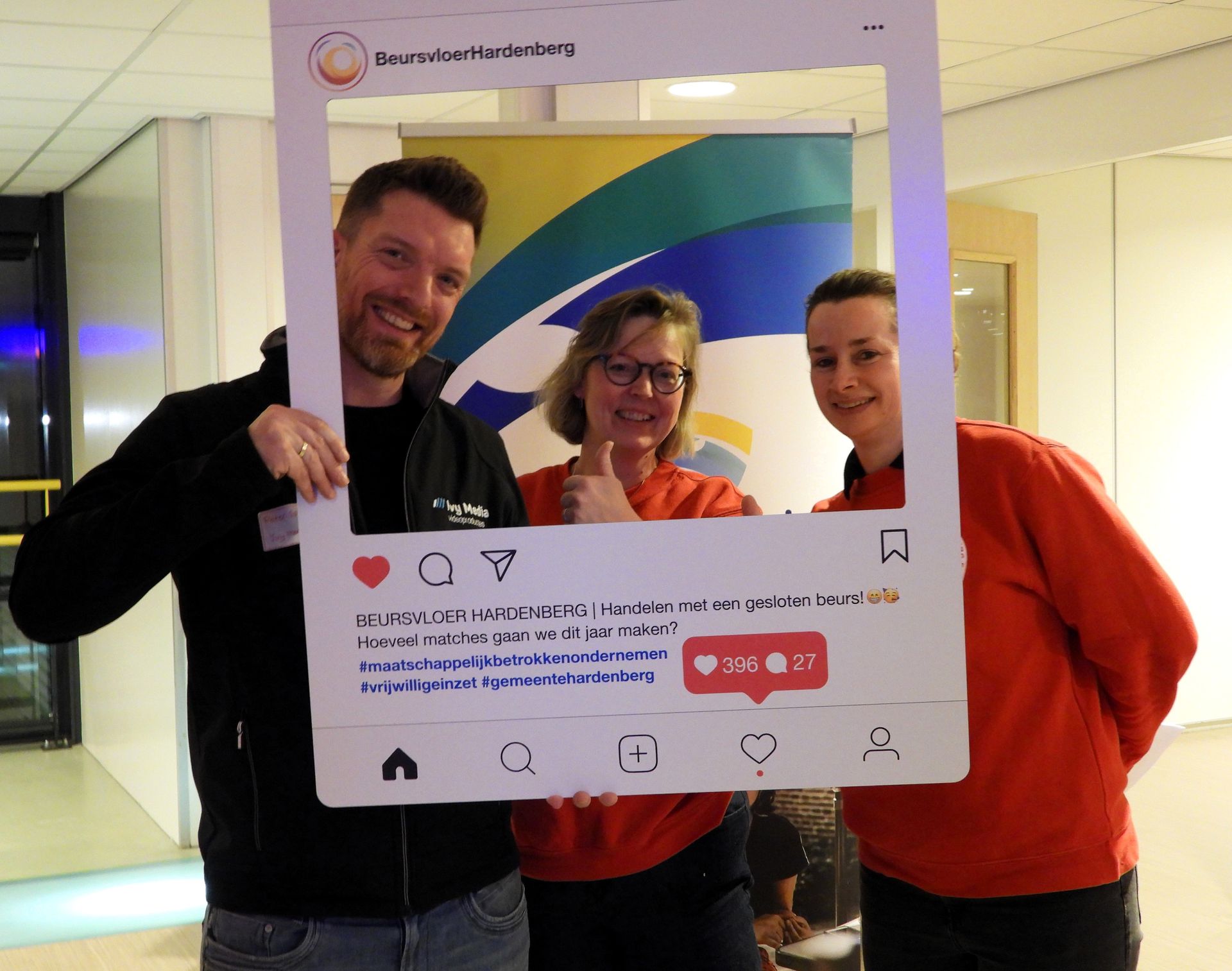 Drie lachende mensen poseren achter een frame voor sociale media, met een logo op de achtergrond.