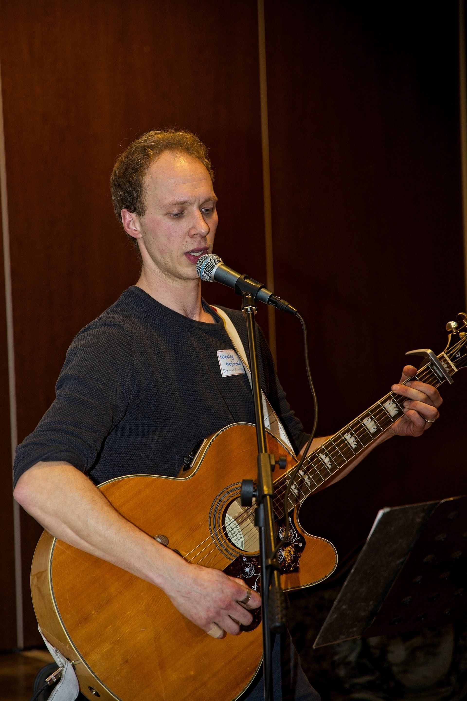 Een man zingt en speelt akoestische gitaar met een microfoon voor zich.