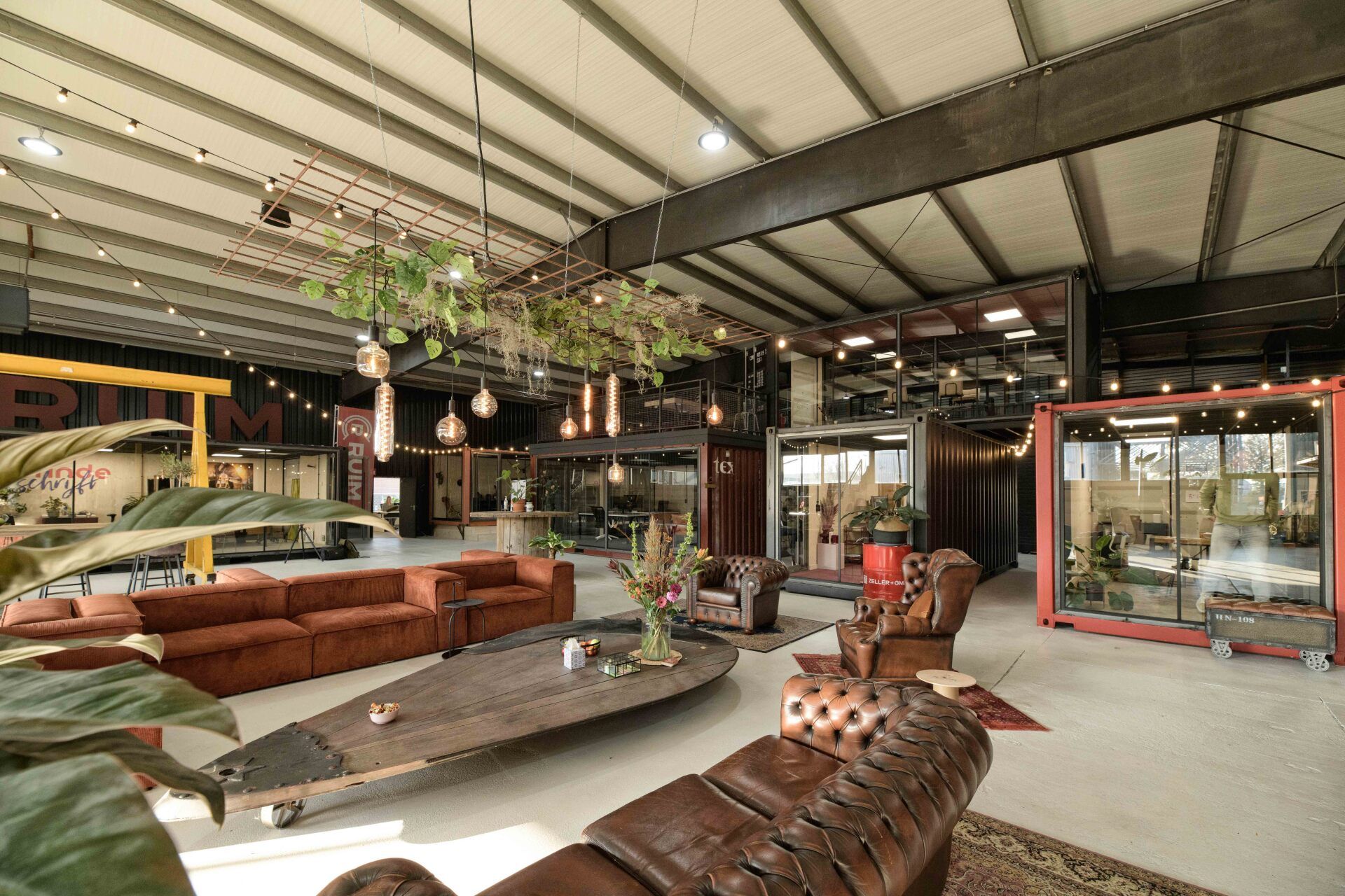 Moderne lounge in industriële stijl met zitgelegenheid, planten en hergebruikte zeecontainers.