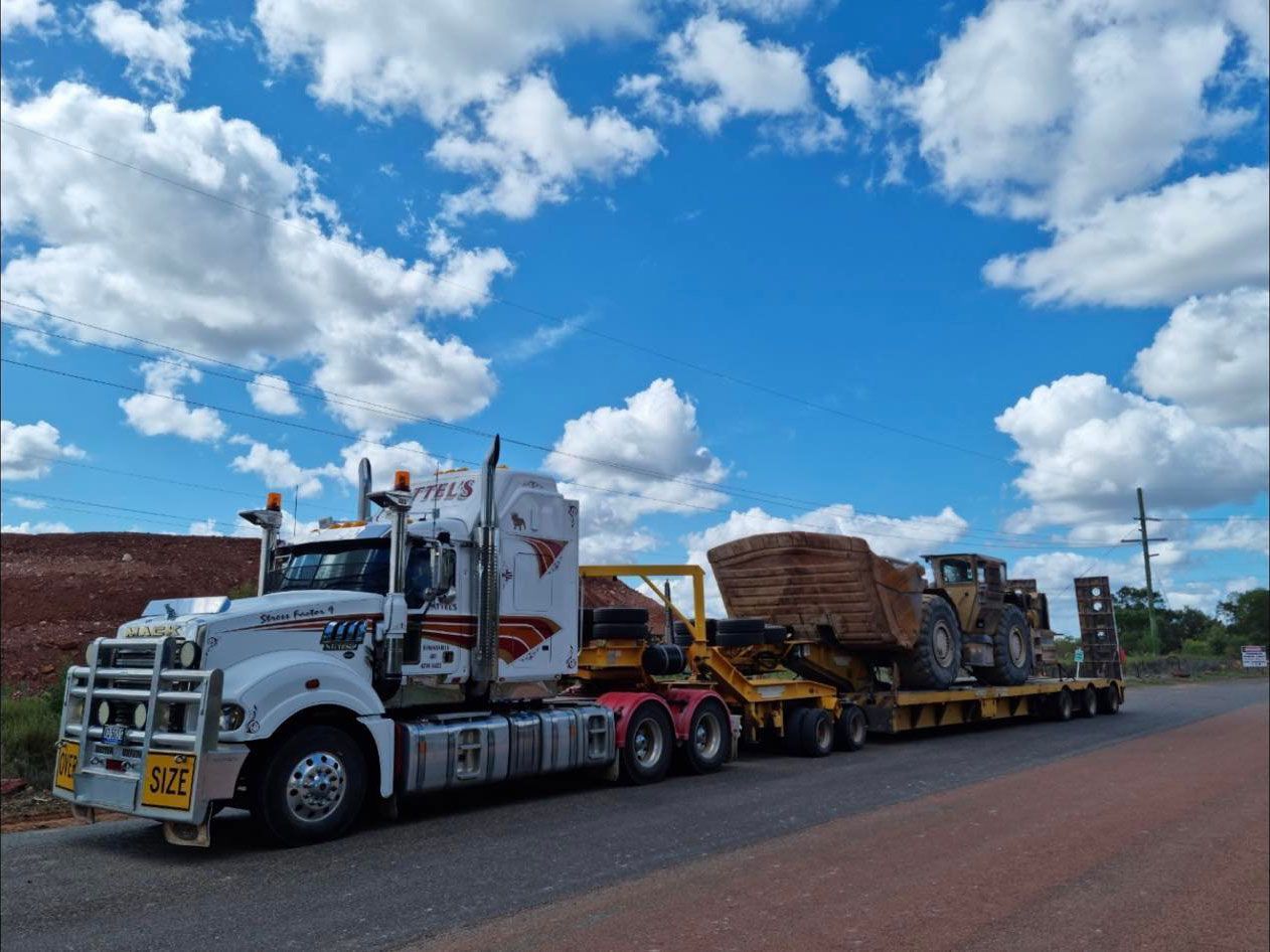 Truck Is Driving Down A Road With A Trailer Carrying A Bulldozer — Pattel's Heavy Haulage Townsville Pty Ltd In Garbutt, QLD