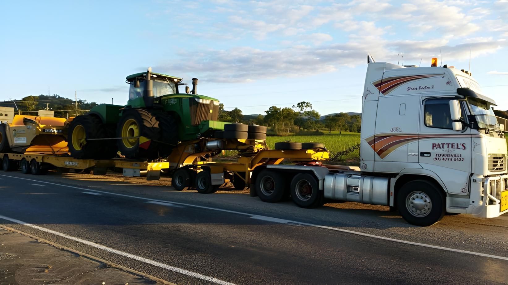 A Semi Truck Is Carrying A Green Tractor On A Trailer — Pattel's Heavy Haulage Townsville Pty Ltd In Garbutt, QLD