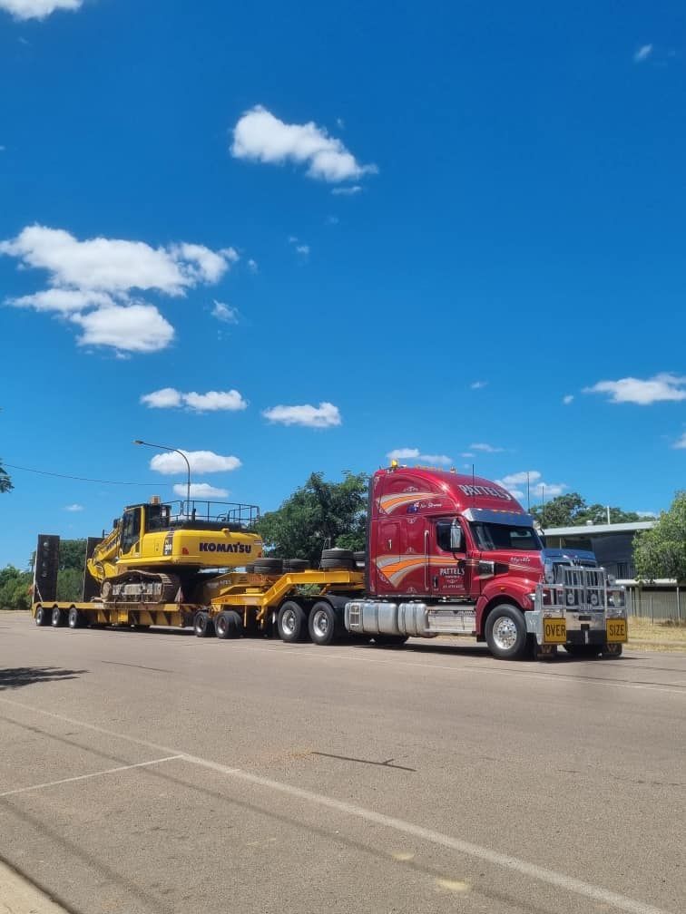 A Red Semi Truck Is Carrying A Yellow Excavator On A Trailer — Pattel's Heavy Haulage Townsville Pty Ltd In Garbutt, QLD