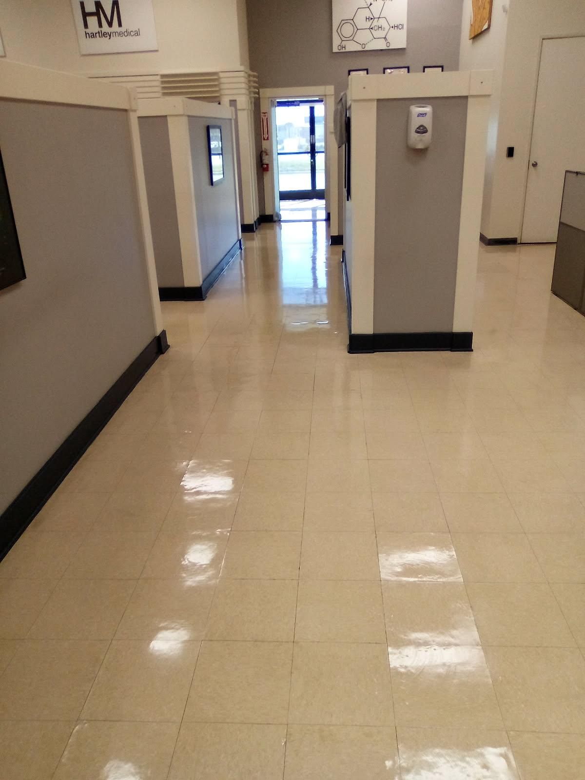 Hallway with gray cubicles, shiny floor, and a glass door at the end.