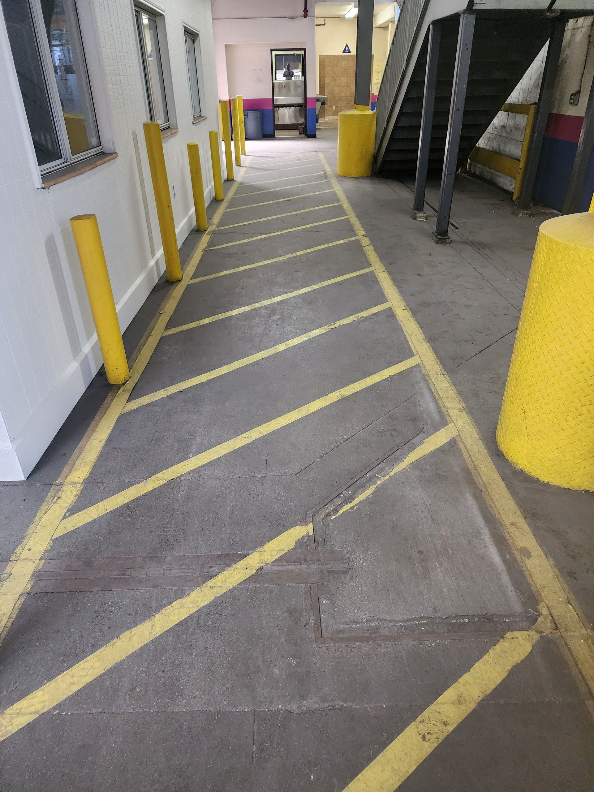 Marked warehouse loading lane with yellow bollards and diagonal striped pavement beside a building.