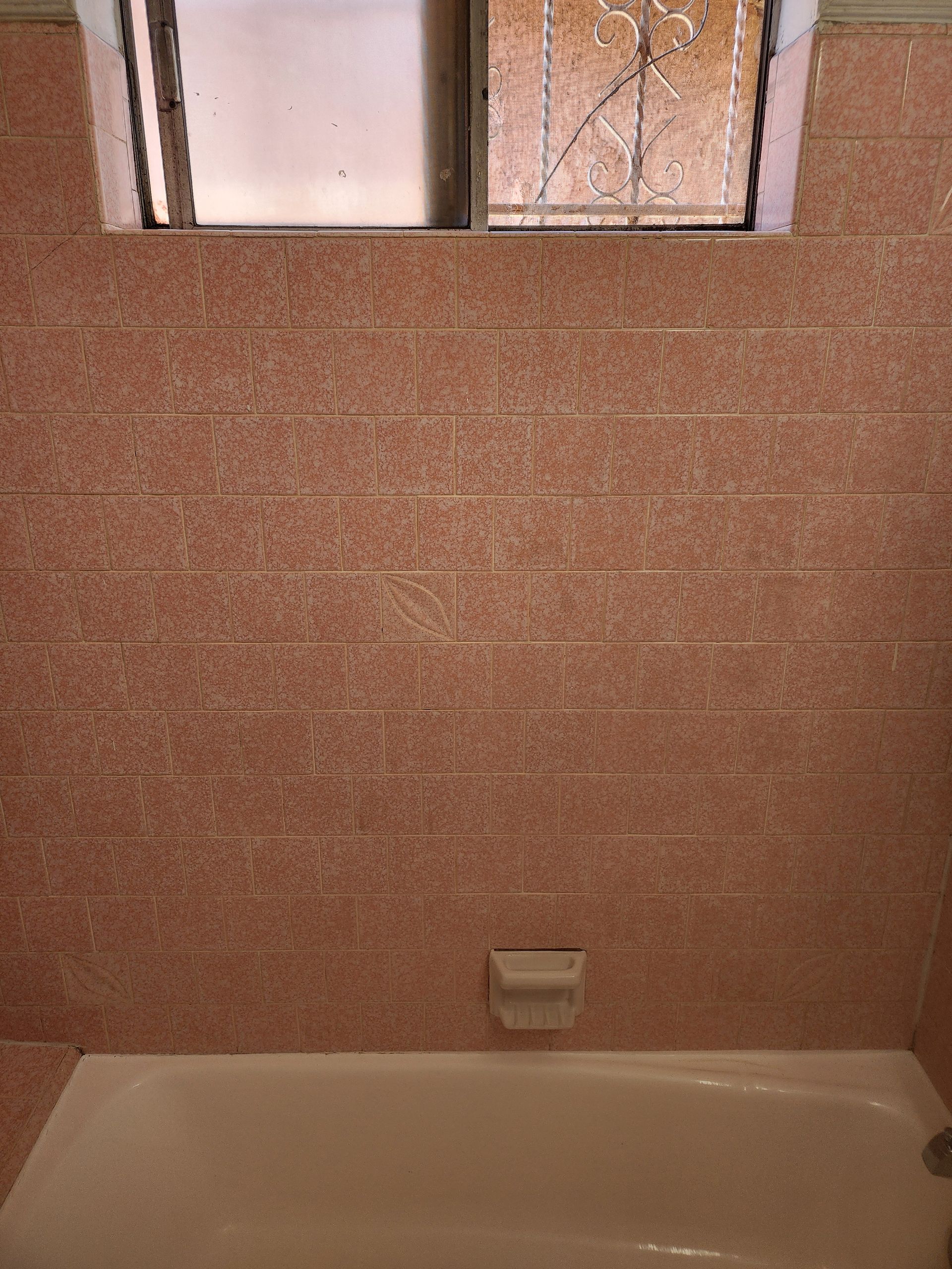 Small bathroom with a beige bathtub, pink tiled wall, and frosted window above.