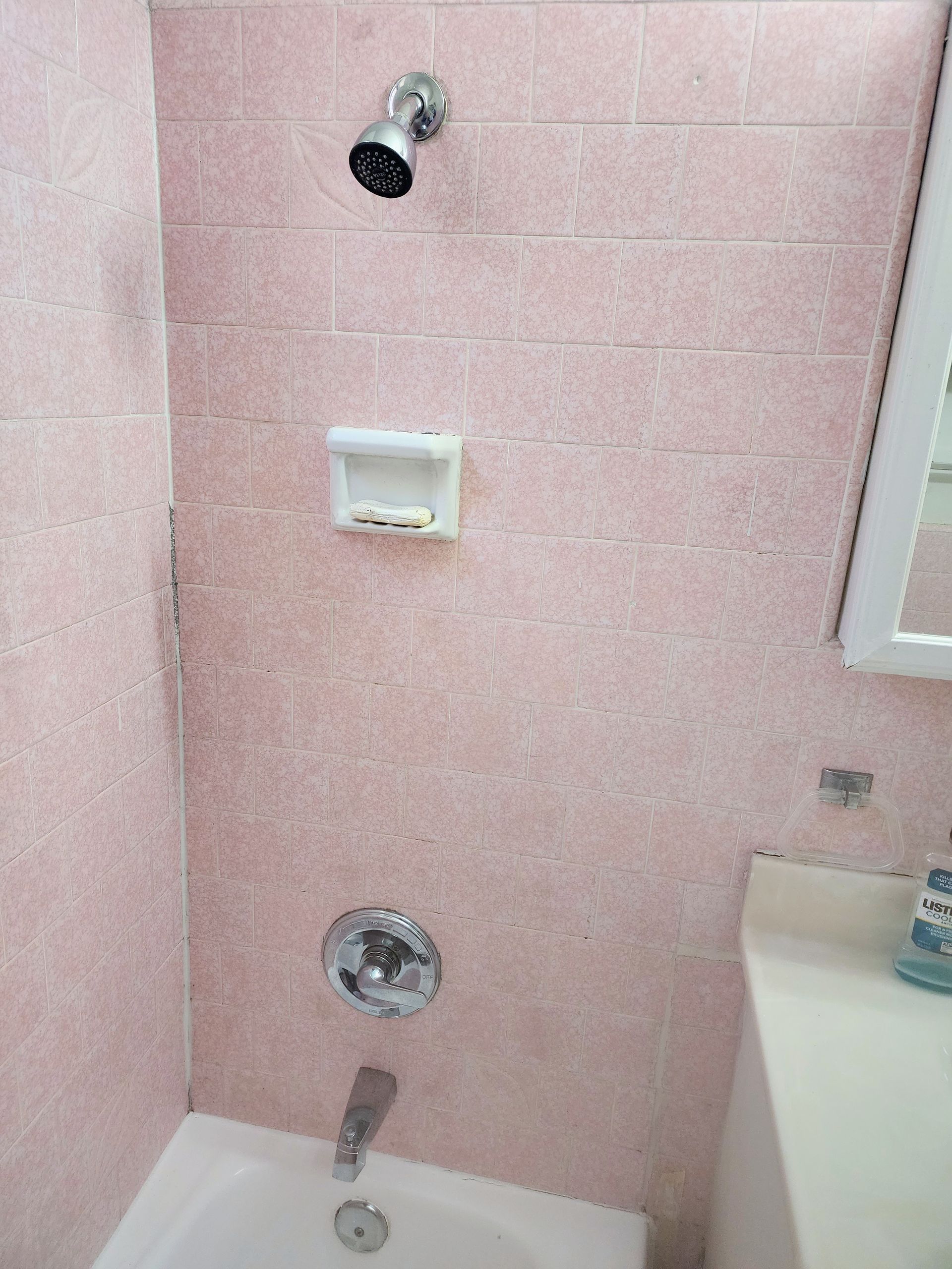 Pink tiled shower with wall-mounted showerhead, soap dish, and faucet above a bathtub.