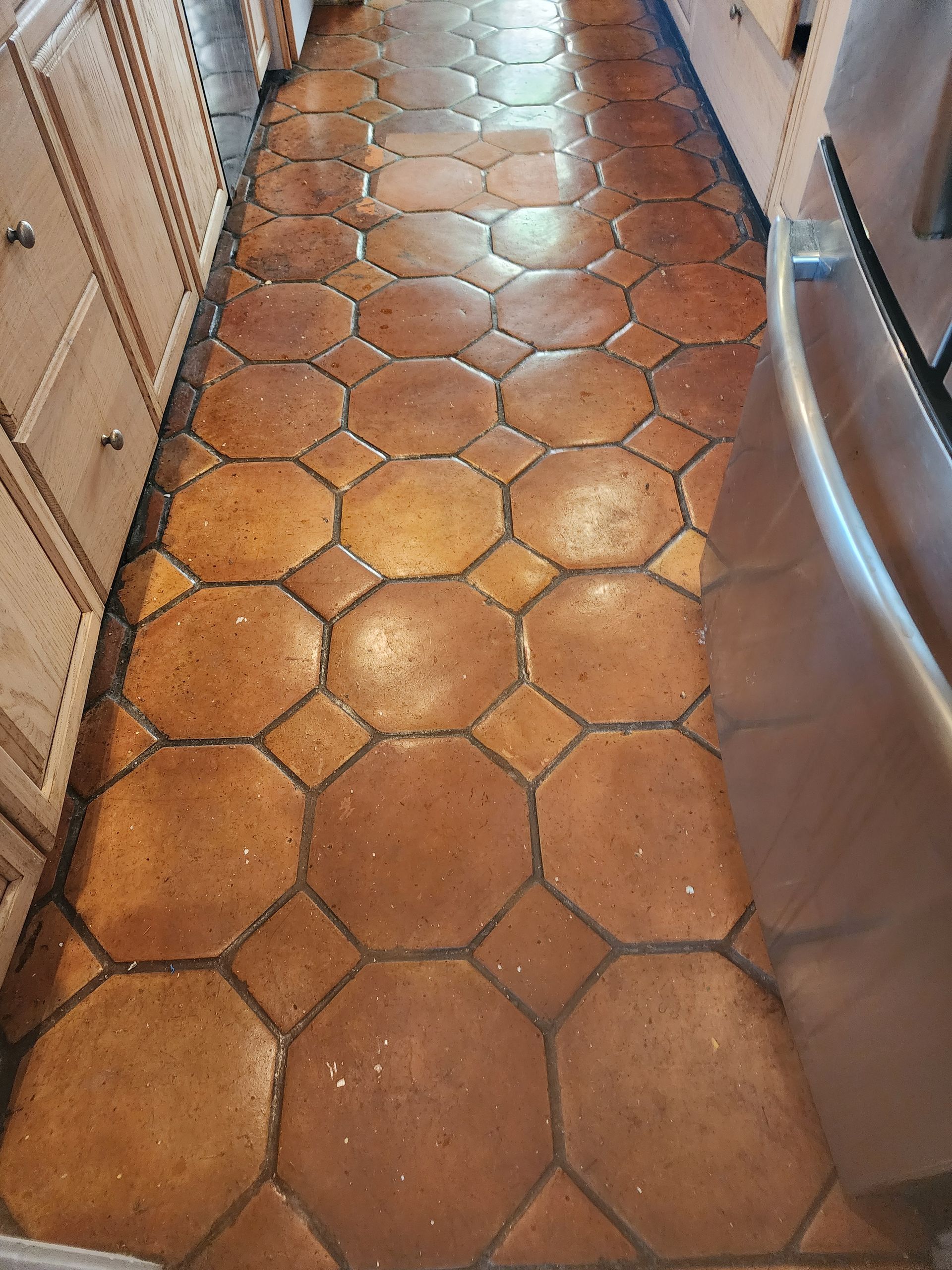 Narrow kitchen hallway with terracotta hex tile floor between cabinets and stainless steel appliances