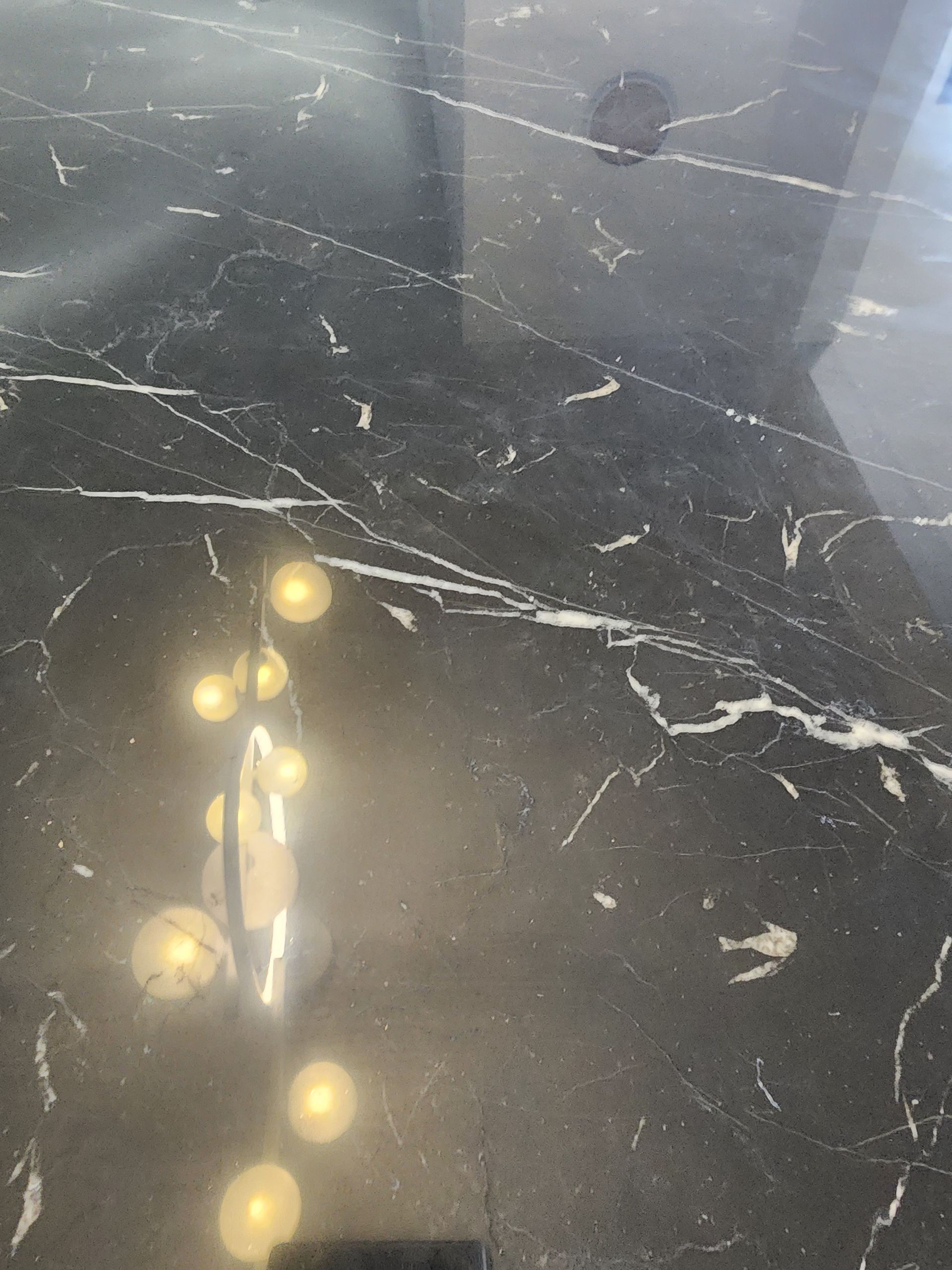 Shiny black marble countertop with white veining and reflected warm lights.