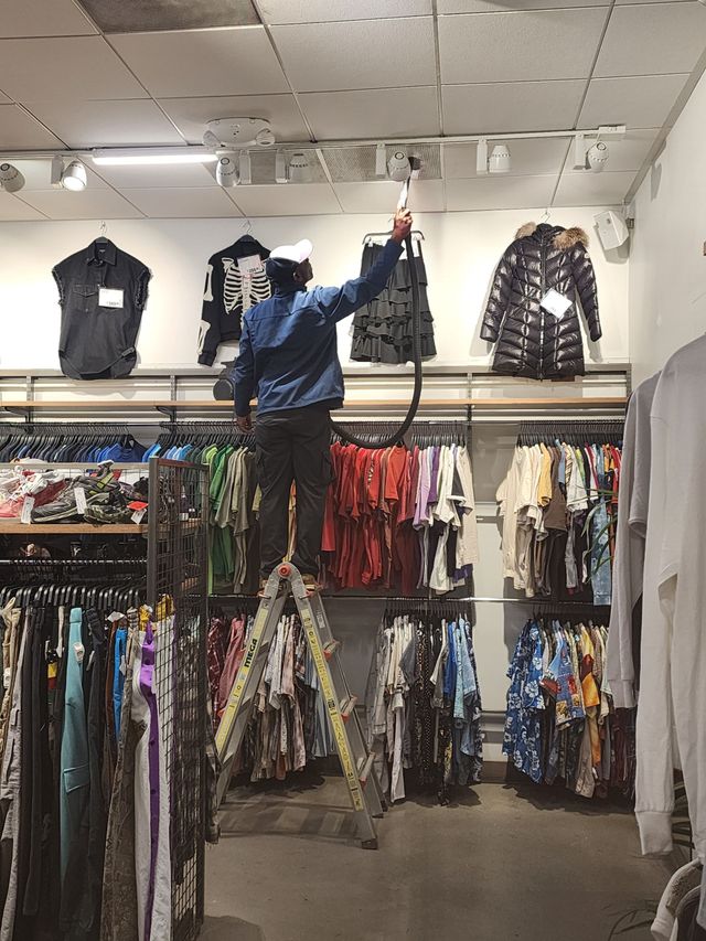 Person reaching for clothing on a high rack in a clothing store aisle