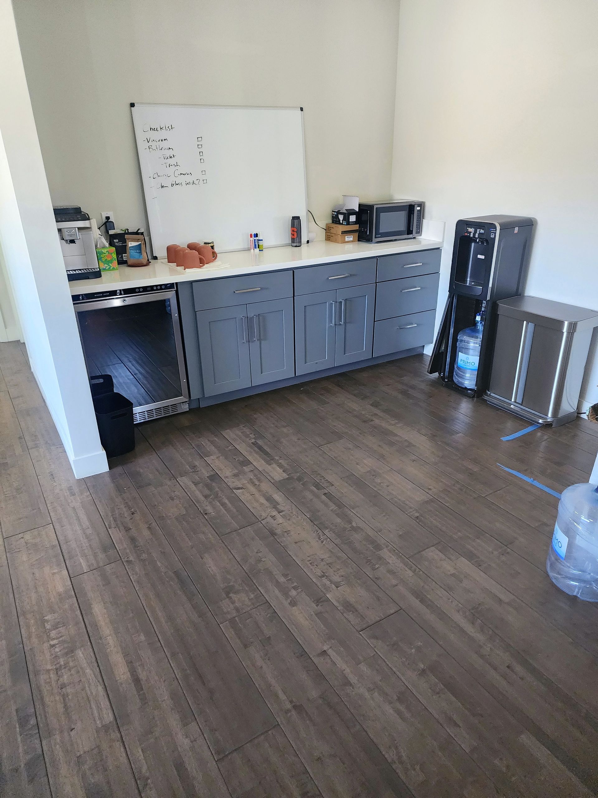 Empty room with gray cabinets, a whiteboard, and a small kitchenette area on wood flooring.